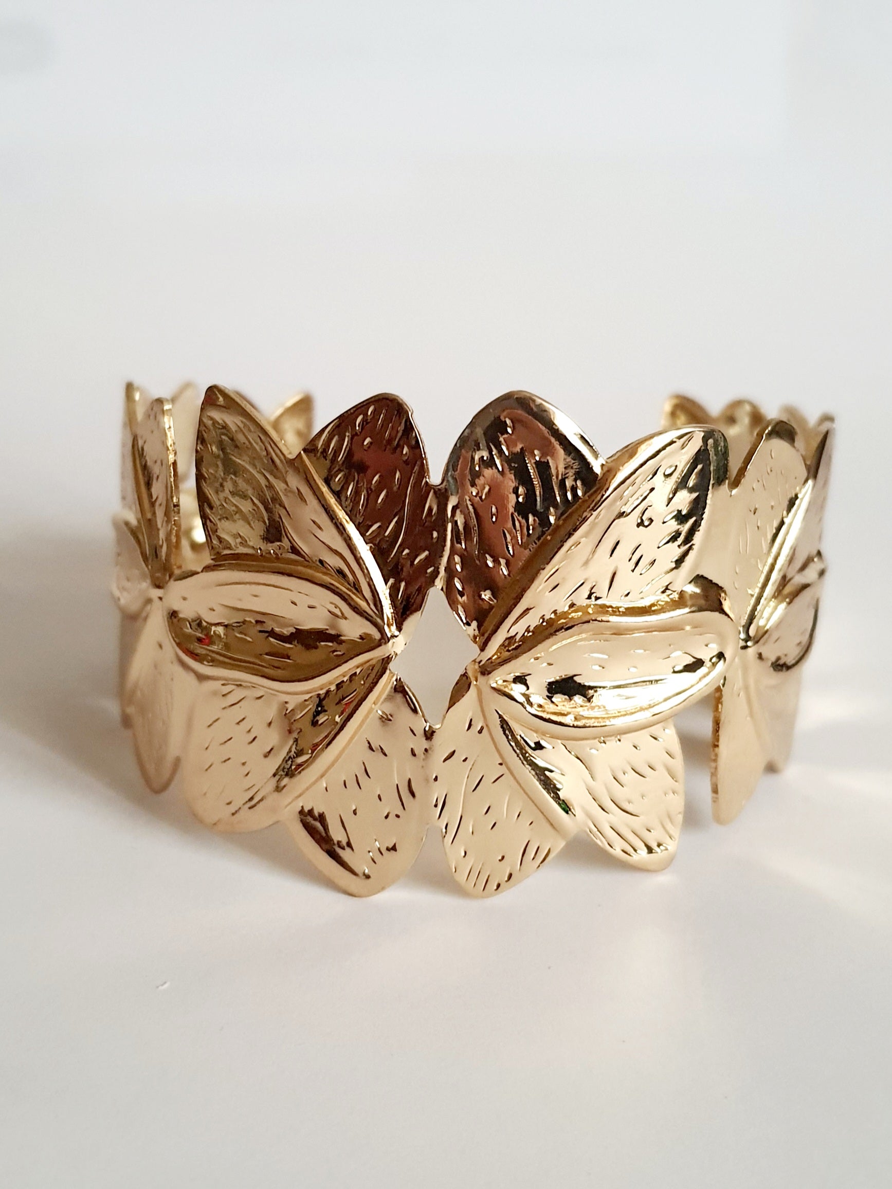 Złota bransoletka ze stali nierdzewnej w formie splecionych liści, inspirowana naturą, elegancka i kobieca, średnica 6 cm. Styl glamour z nutą boho. Rouge Bizu.