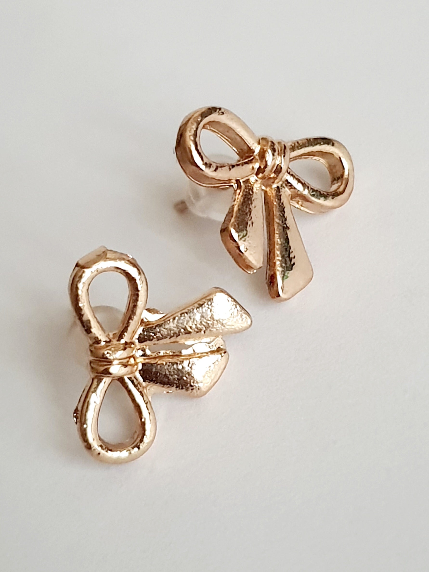 Złote kolczyki kokardki wkrętki, stal nierdzewna, długość 1,5 cm, subtelny romantyczny styl. Rouge Bizu.