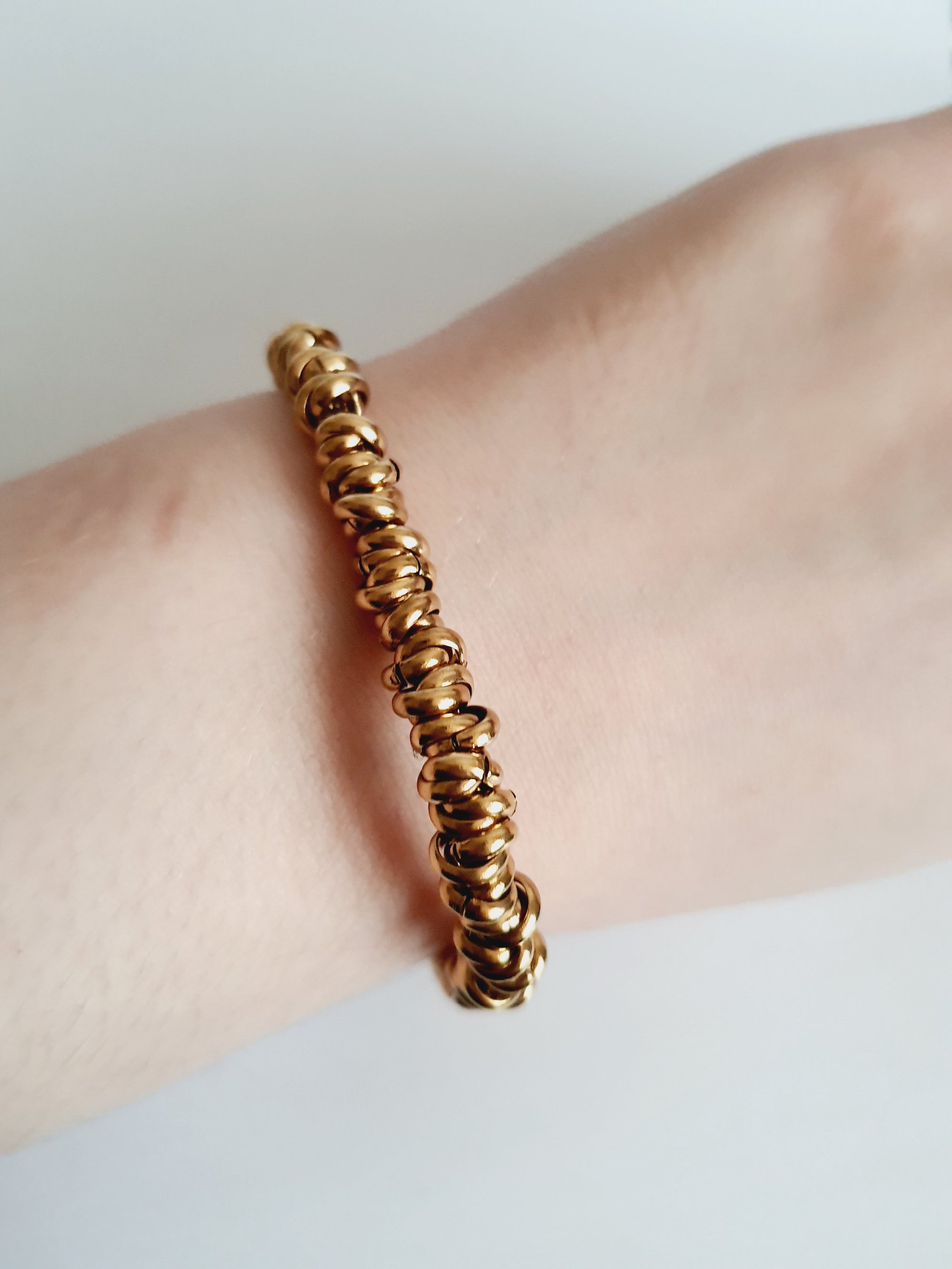 Złota bransoletka ze stali nierdzewnej, masywna forma ze splecionymi elementami, długość regulowana 18–24 cm, elegancki styl glamour. Rouge Bizu.