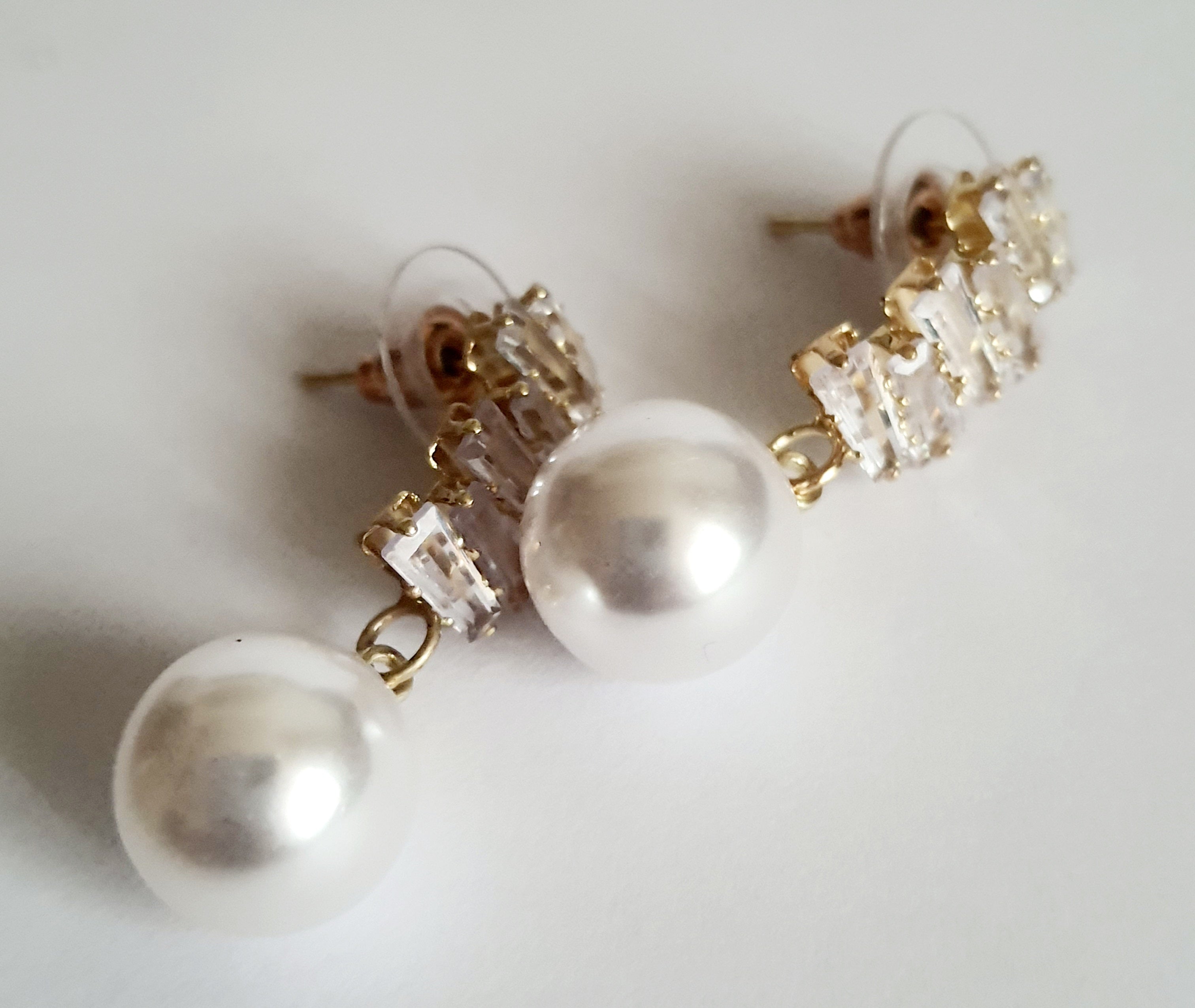 Złote kolczyki ze stali nierdzewnej z cyrkoniami i dużą perłą syntetyczną, długość 3 cm, elegancki styl glamour. Rouge Bizu.