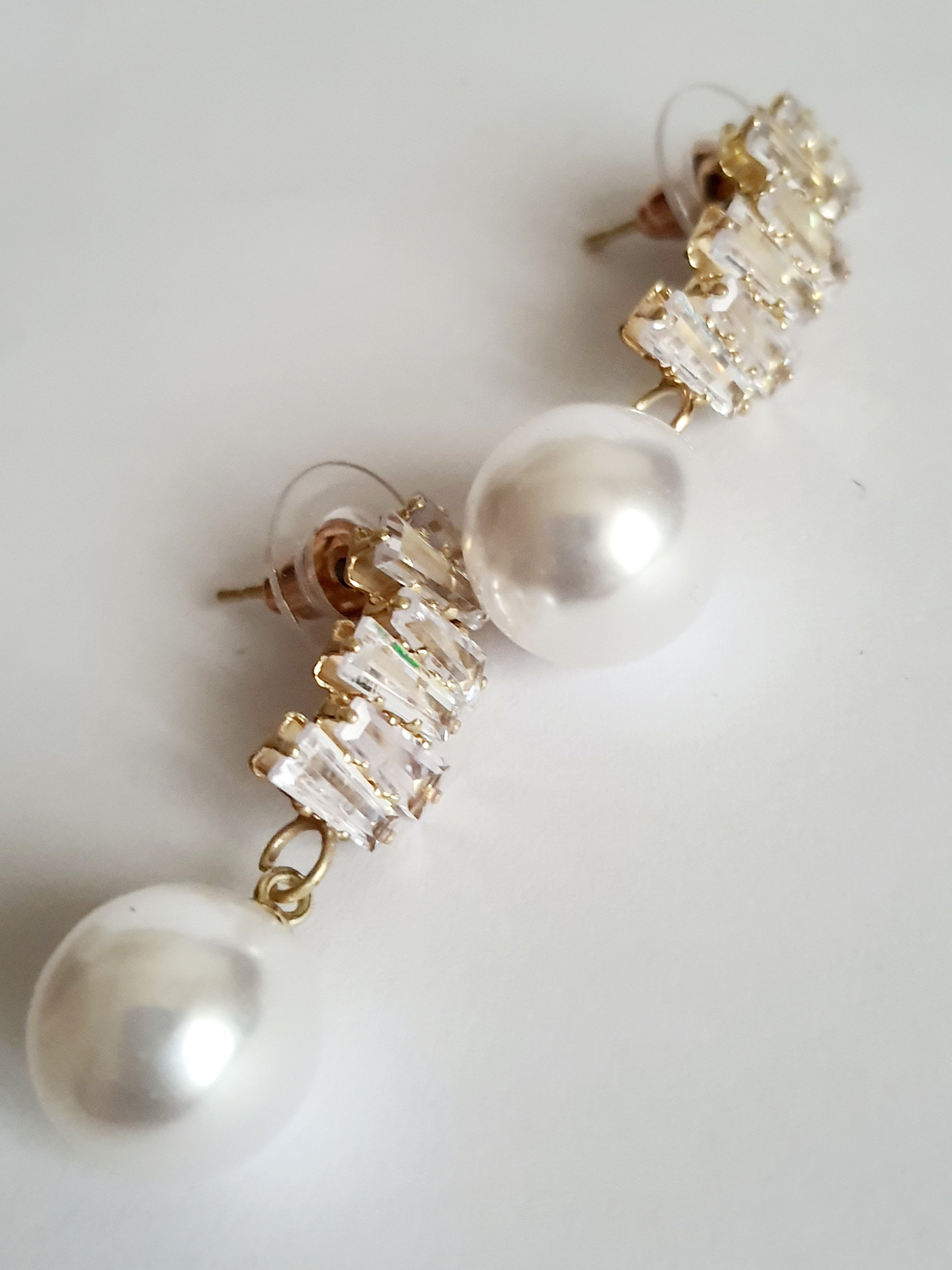 Złote kolczyki ze stali nierdzewnej z cyrkoniami i dużą perłą syntetyczną, długość 3 cm, elegancki styl glamour. Rouge Bizu.