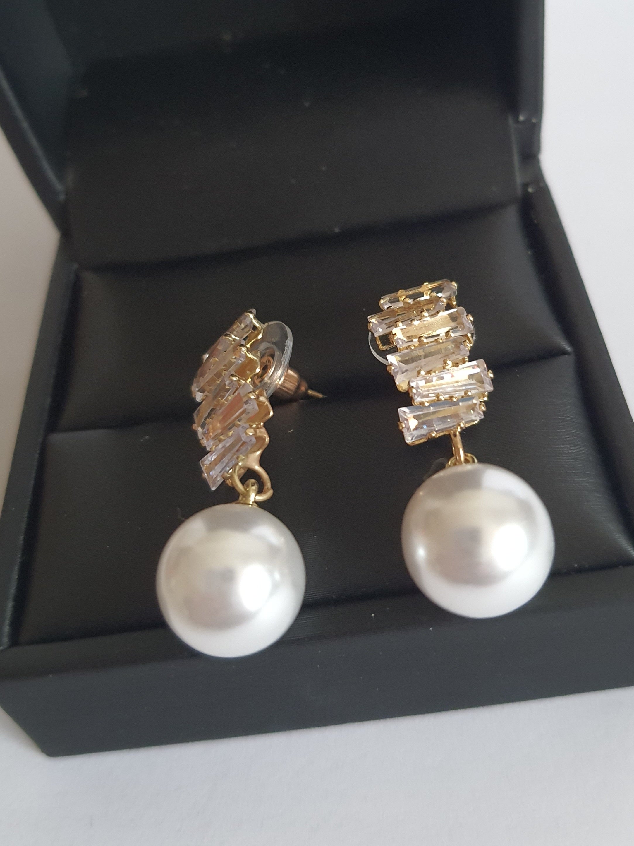 Złote kolczyki ze stali nierdzewnej z cyrkoniami i dużą perłą syntetyczną, długość 3 cm, elegancki styl glamour. Rouge Bizu.