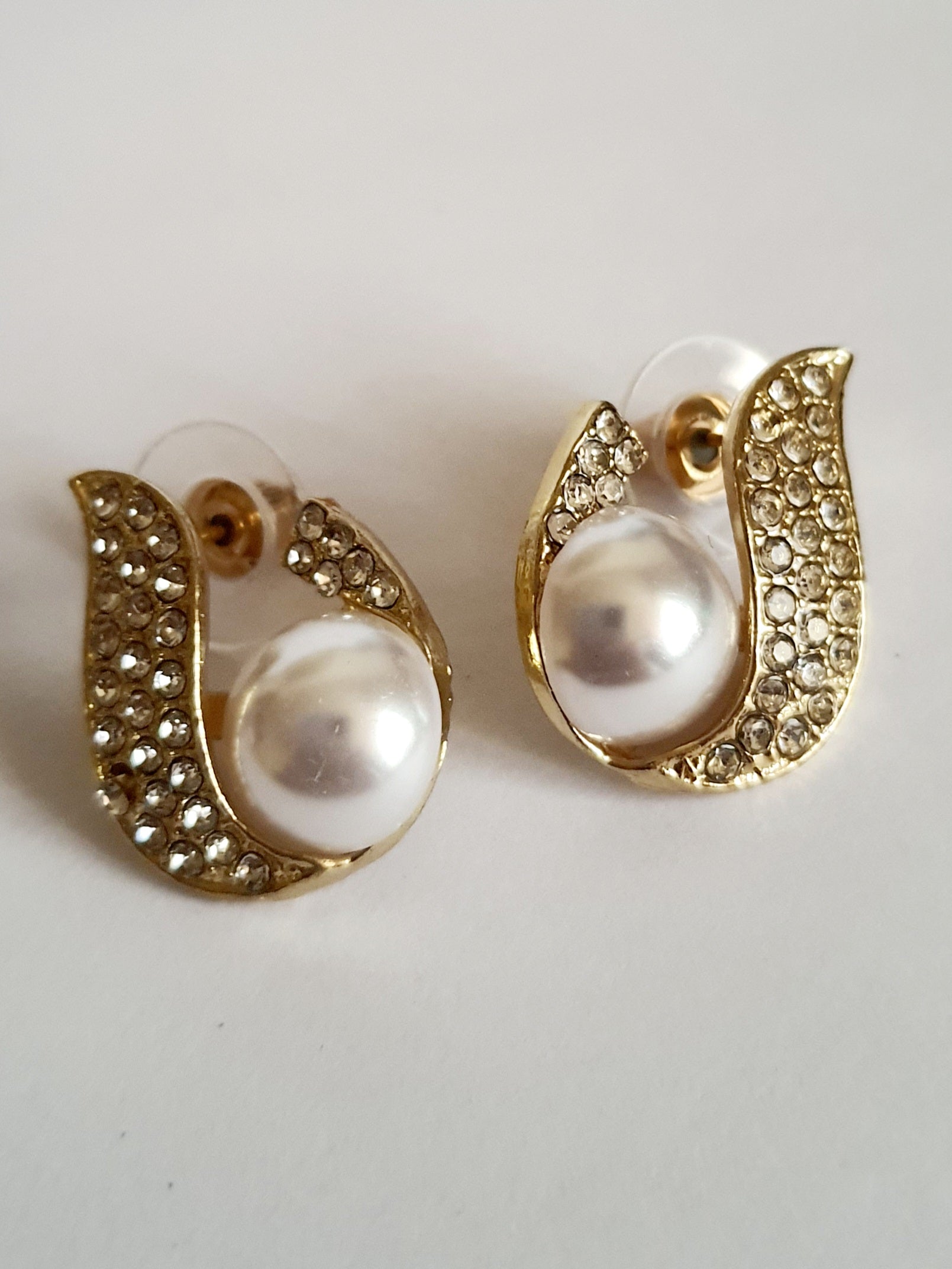 Kolczyki złote ze stali nierdzewnej o długości 2 cm, z białą perłą i oprawą wysadzaną cyrkoniami, elegancki kształt z falującą linią, Rouge Bizu.