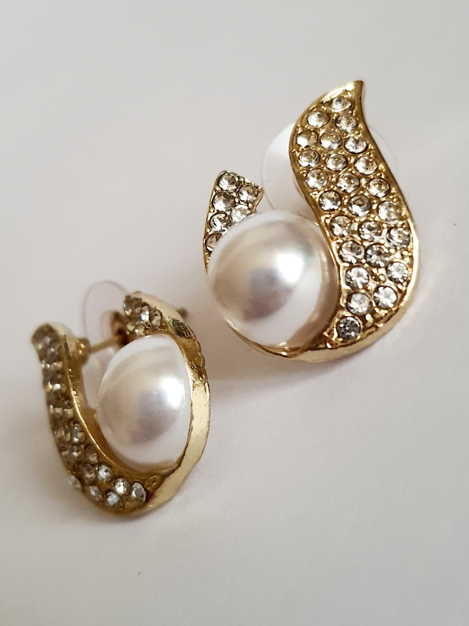 Kolczyki złote ze stali nierdzewnej o długości 2 cm, z białą perłą i oprawą wysadzaną cyrkoniami, elegancki kształt z falującą linią, Rouge Bizu.