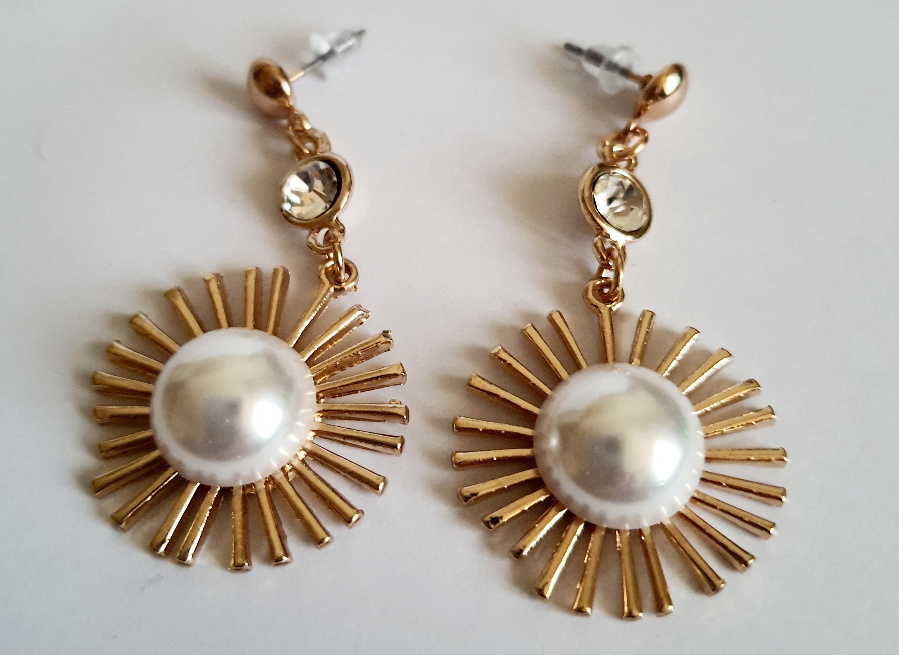 Złote kolczyki wiszące 5 cm, z białą perłą w centrum i promienistą oprawą, u góry kryształek – elegancki design inspirowany słońcem, Rouge Bizu.