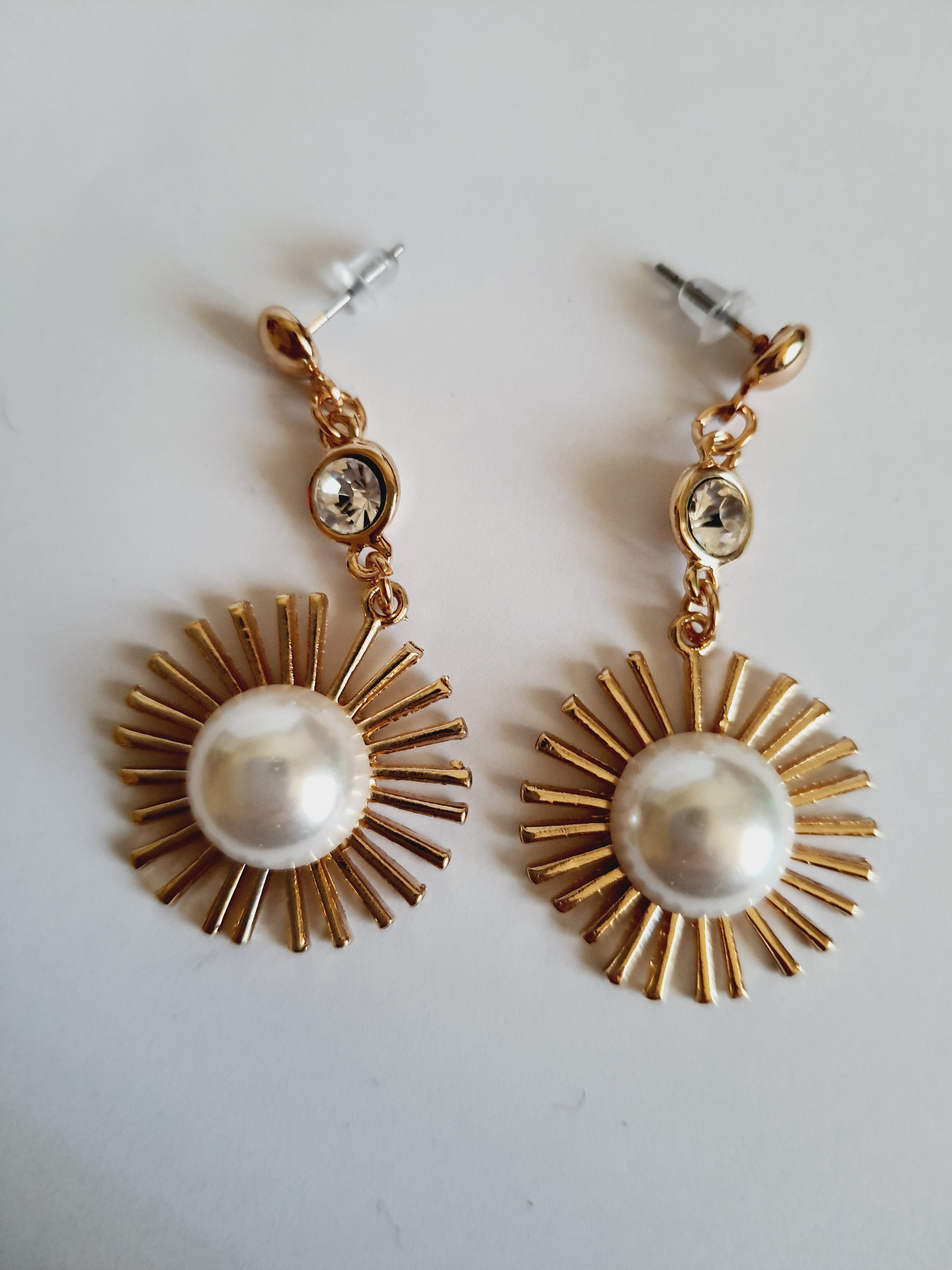 Złote kolczyki wiszące 5 cm, z białą perłą w centrum i promienistą oprawą, u góry kryształek – elegancki design inspirowany słońcem, Rouge Bizu.