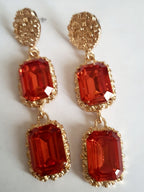 Długie kolczyki ze stali nierdzewnej w stylu glamour, ozdobione dużymi czerwonymi kamieniami w złotej oprawie. Elegancja, luksus i ognisty blask. Długość 7 cm. Rouge Bizu.