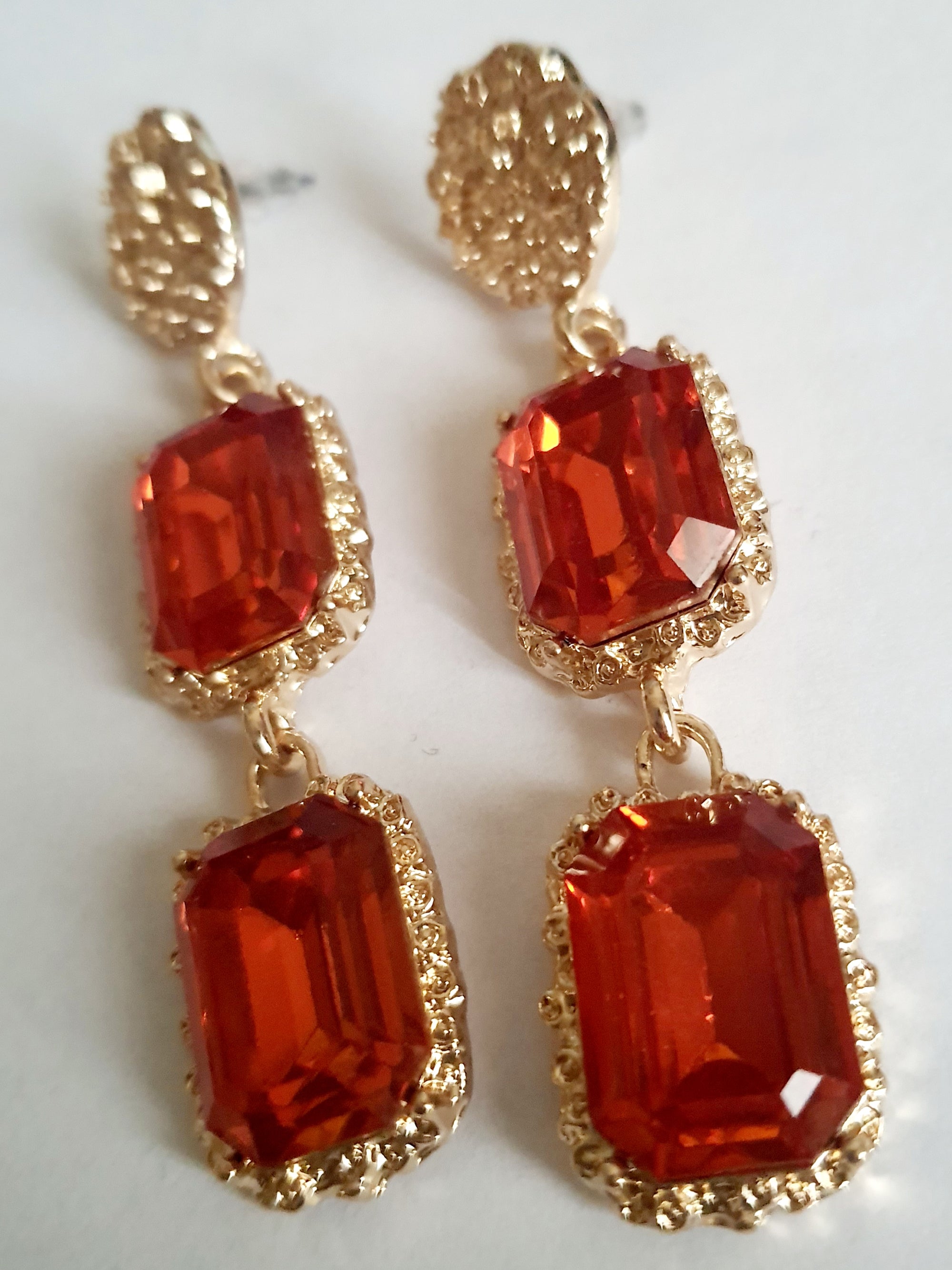 Długie kolczyki ze stali nierdzewnej w stylu glamour, ozdobione dużymi czerwonymi kamieniami w złotej oprawie. Elegancja, luksus i ognisty blask. Długość 7 cm. Rouge Bizu.