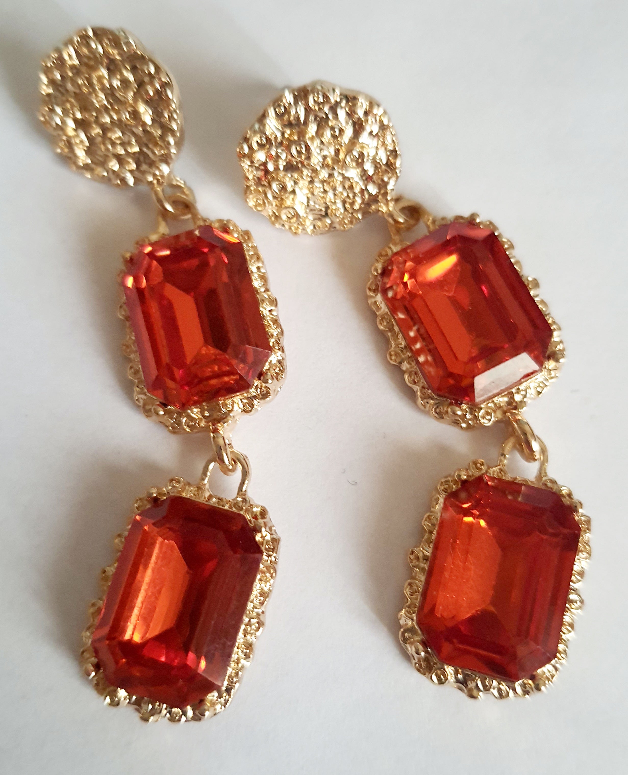 Długie kolczyki ze stali nierdzewnej w stylu glamour, ozdobione dużymi czerwonymi kamieniami w złotej oprawie. Elegancja, luksus i ognisty blask. Długość 7 cm. Rouge Bizu.