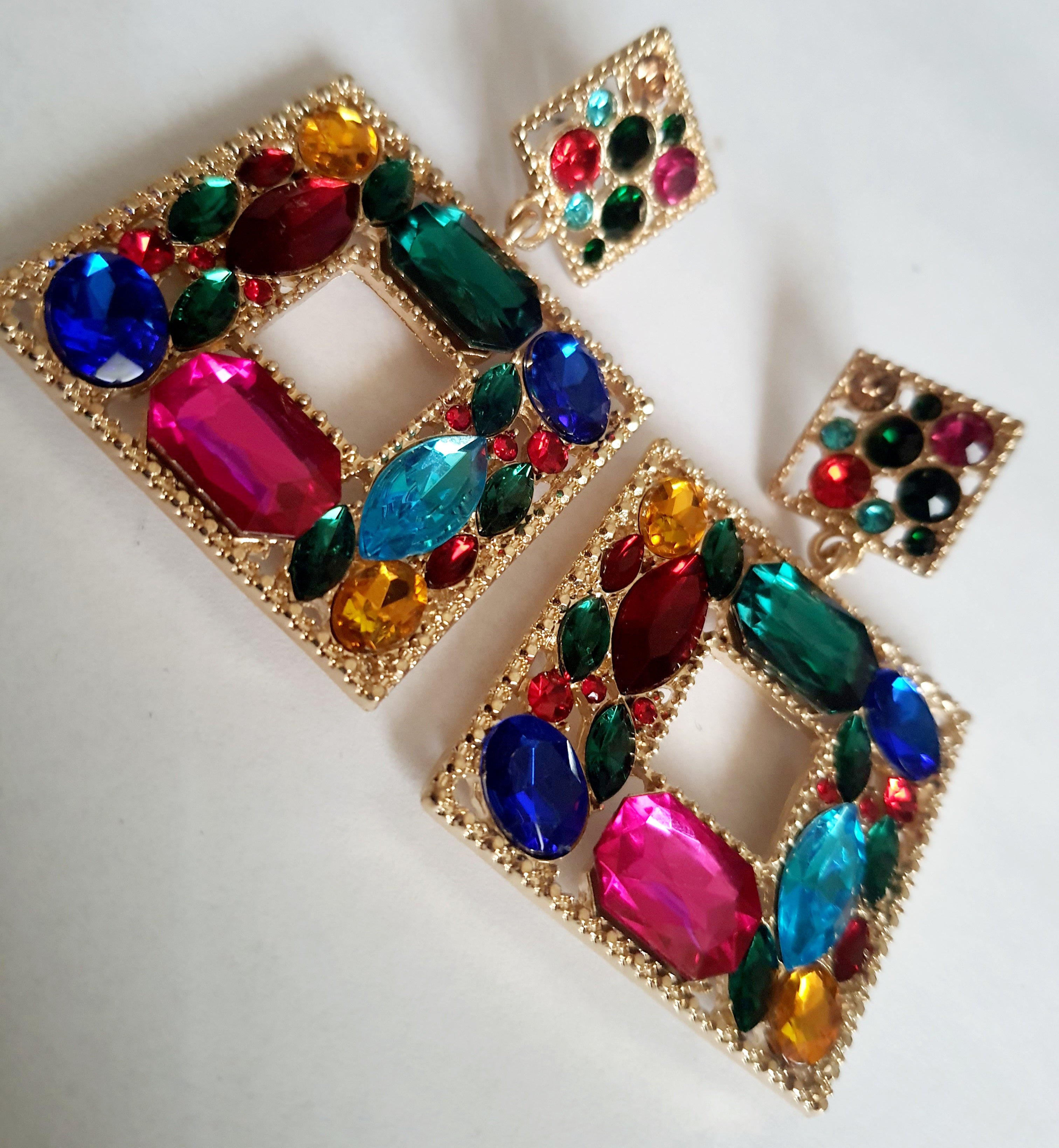 Złote kolczyki ze stali nierdzewnej w kształcie kwadratu, bogato zdobione wielobarwnymi kryształami w odcieniach granatu, zieleni, różu, czerwieni, turkusu i złota. Styl glamour, długość 6 cm. Rouge Bizu.