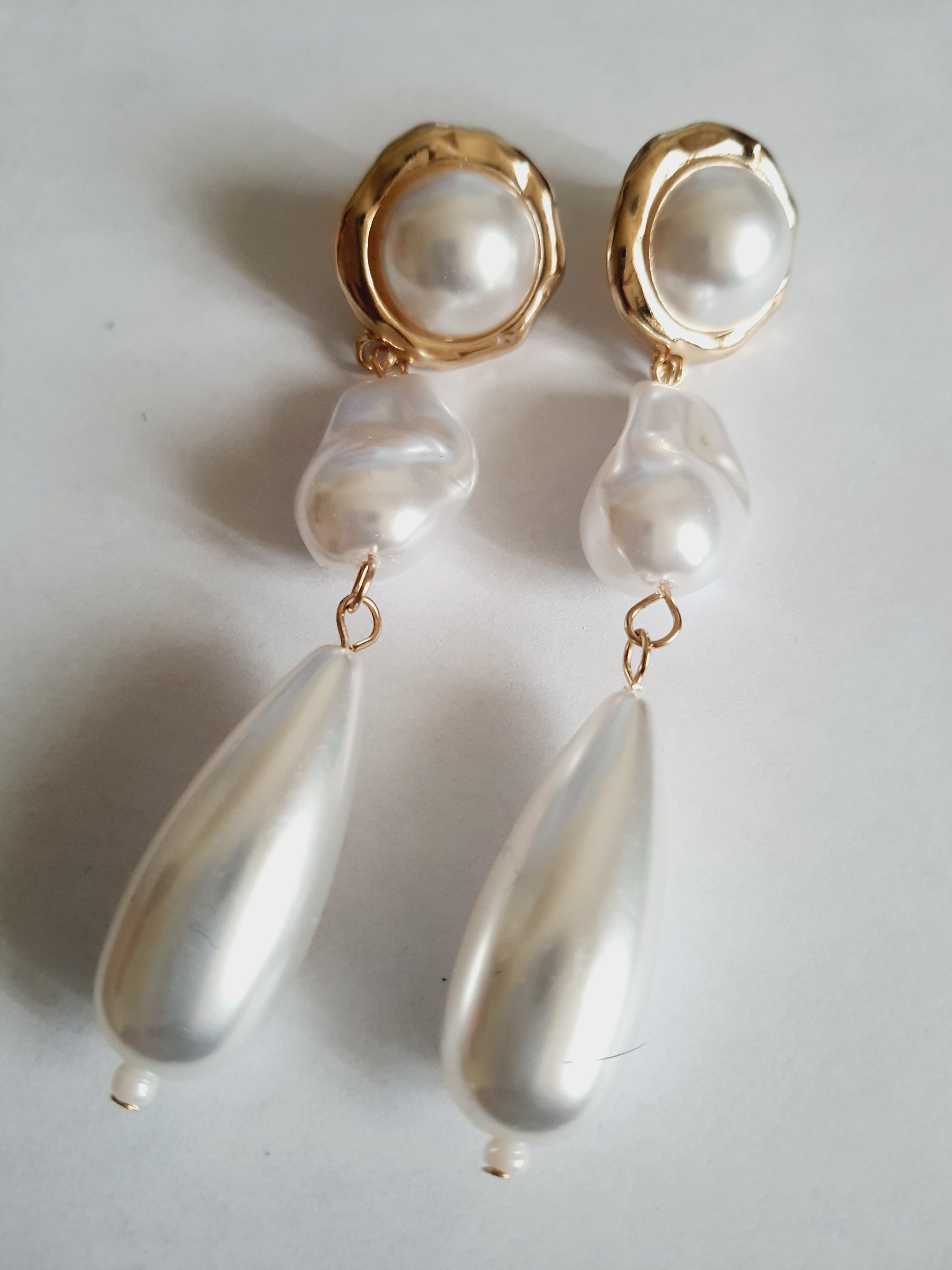 Długie złote kolczyki ze stali nierdzewnej z potrójnymi perłami: okrągłą, nieregularną i kroplą. Styl glamour, klasyczna elegancja. Długość 9 cm. Rouge Bizu.