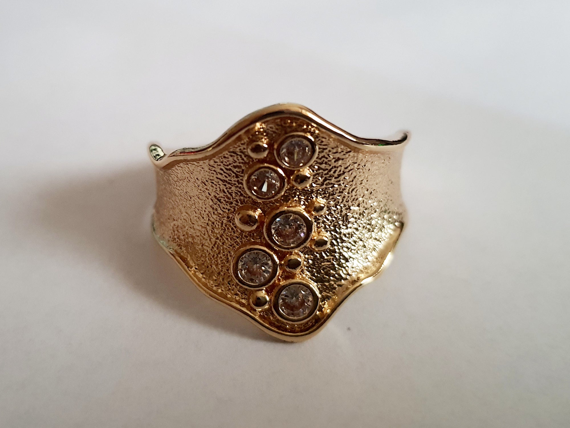 Szeroki złoty pierścionek ze stali nierdzewnej o młotkowanej fakturze, ozdobiony rzędem przezroczystych cyrkonii. Styl glamour, elegancja. Rozmiar 21 mm. Rouge Bizu.