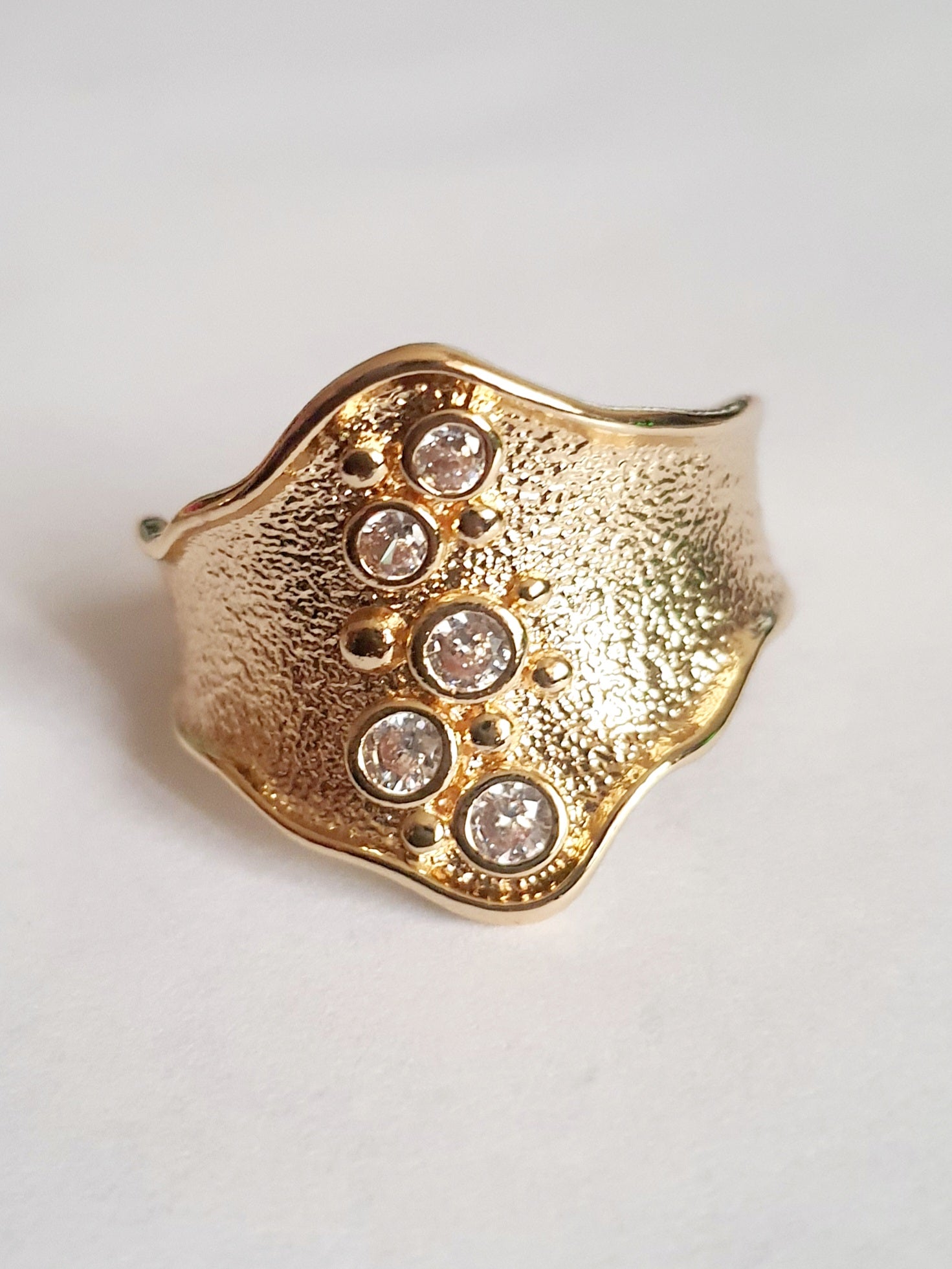 Szeroki złoty pierścionek ze stali nierdzewnej o młotkowanej fakturze, ozdobiony rzędem przezroczystych cyrkonii. Styl glamour, elegancja. Rozmiar 21 mm. Rouge Bizu.