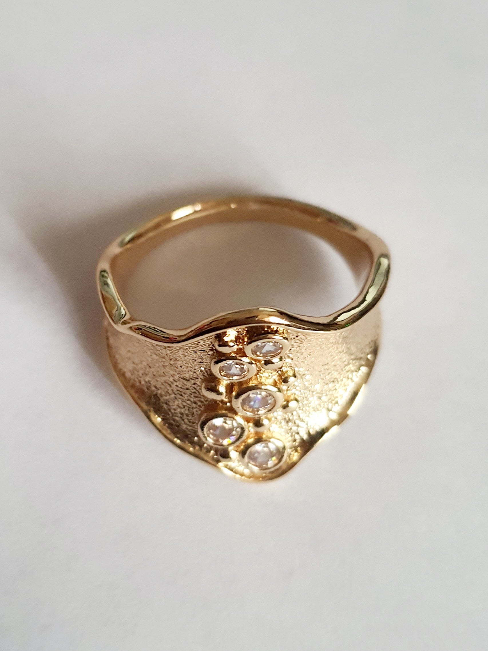 Szeroki złoty pierścionek ze stali nierdzewnej o młotkowanej fakturze, ozdobiony rzędem przezroczystych cyrkonii. Styl glamour, elegancja. Rozmiar 21 mm. Rouge Bizu.