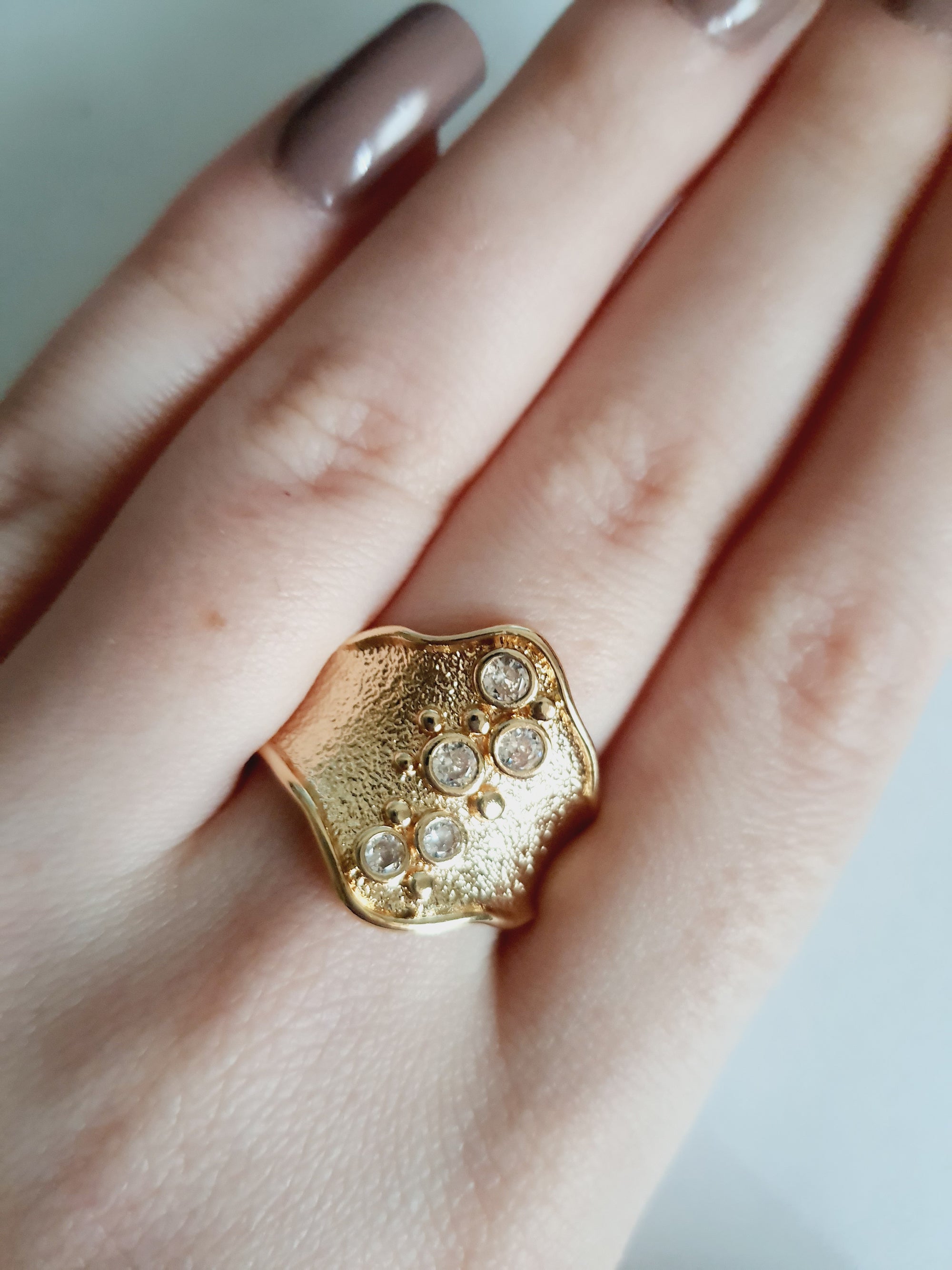 Szeroki złoty pierścionek ze stali nierdzewnej o młotkowanej fakturze, ozdobiony rzędem przezroczystych cyrkonii. Styl glamour, elegancja. Rozmiar 21 mm. Rouge Bizu.