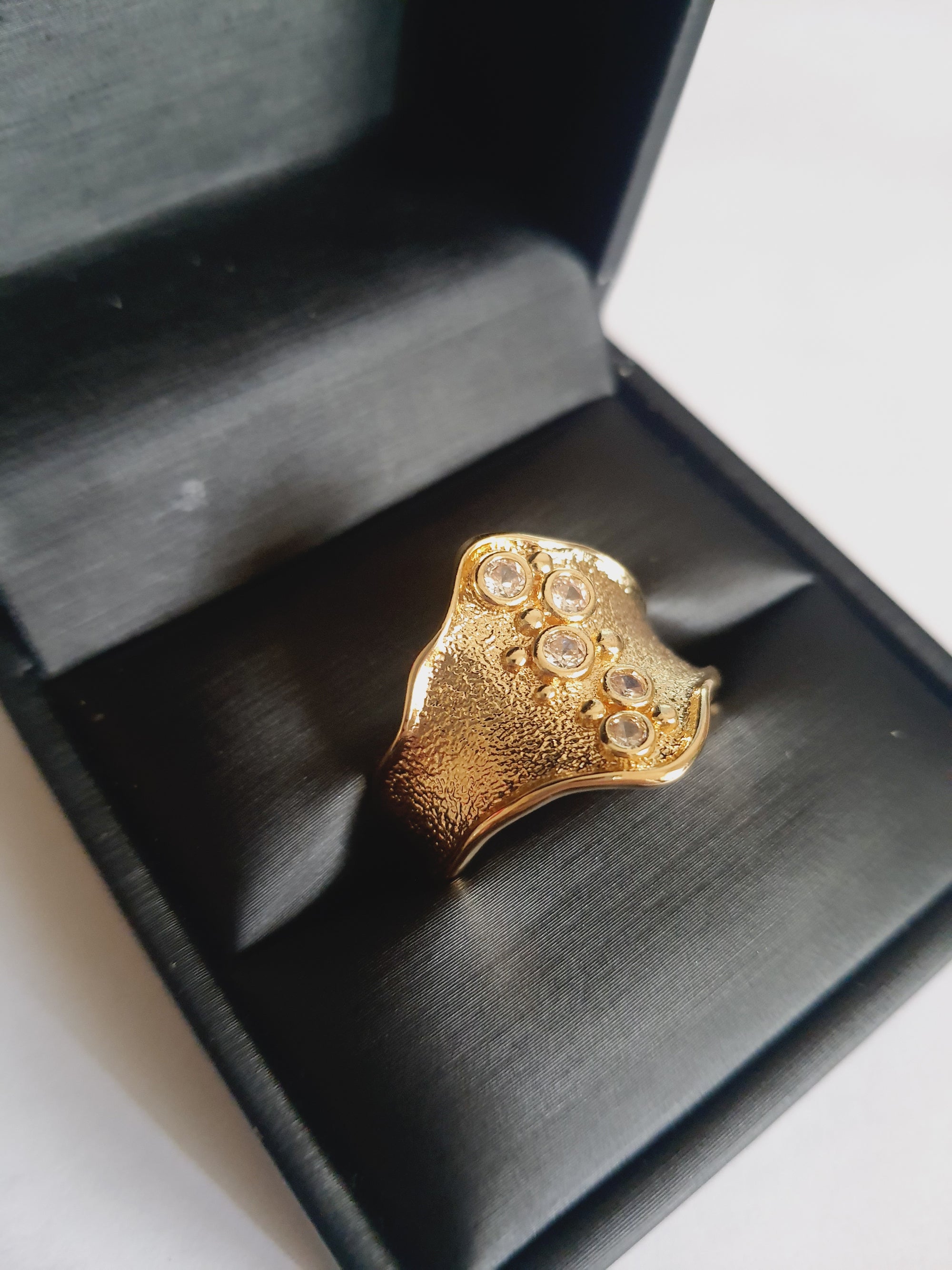 Szeroki złoty pierścionek ze stali nierdzewnej o młotkowanej fakturze, ozdobiony rzędem przezroczystych cyrkonii. Styl glamour, elegancja. Rozmiar 21 mm. Rouge Bizu.