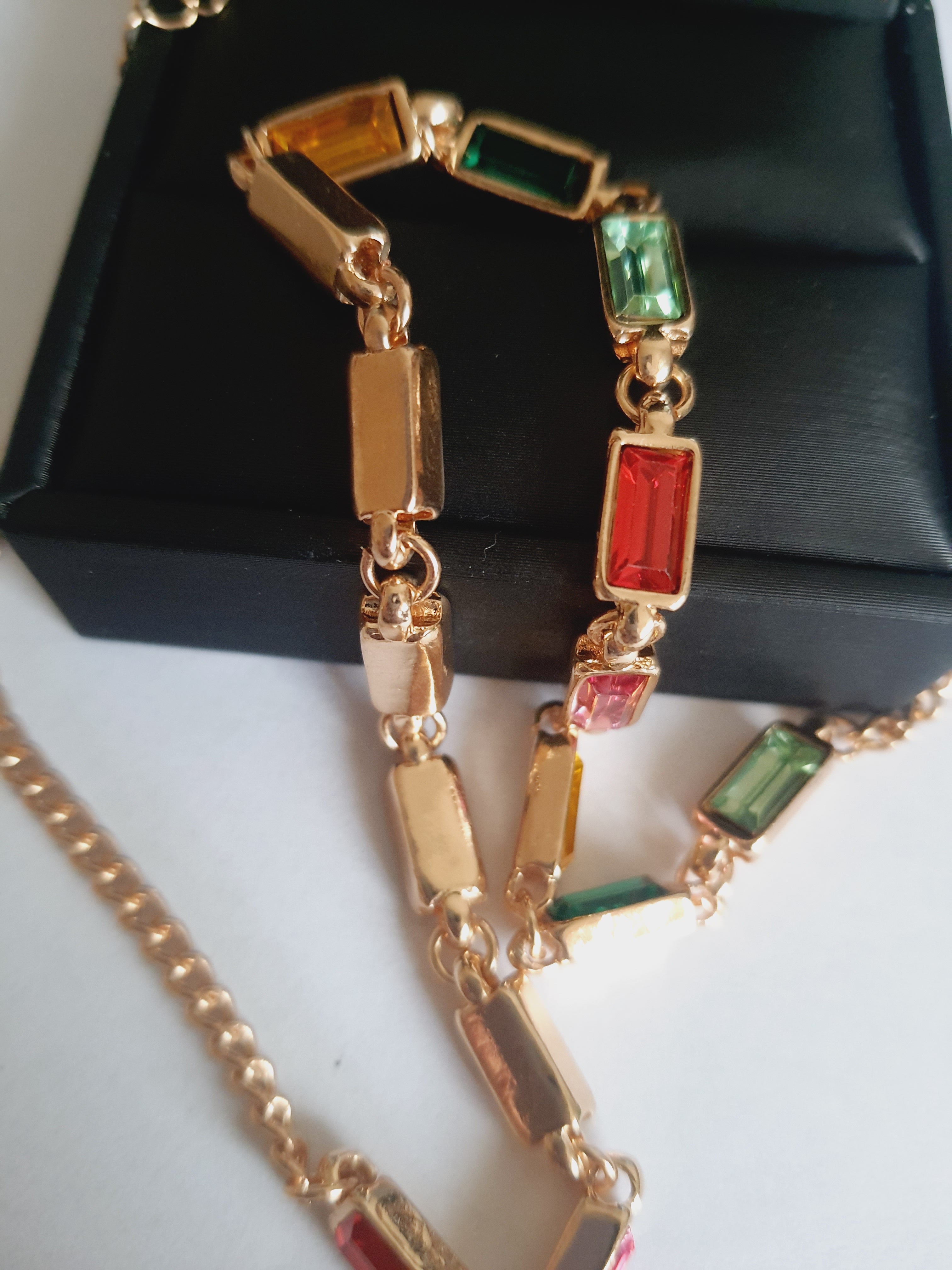 Złoty naszyjnik ze stali nierdzewnej z prostokątnymi, wielobarwnymi kryształami w odcieniach zieleni, czerwieni, różu, złota i turkusu. Długość 41–47 cm. Rouge Bizu.