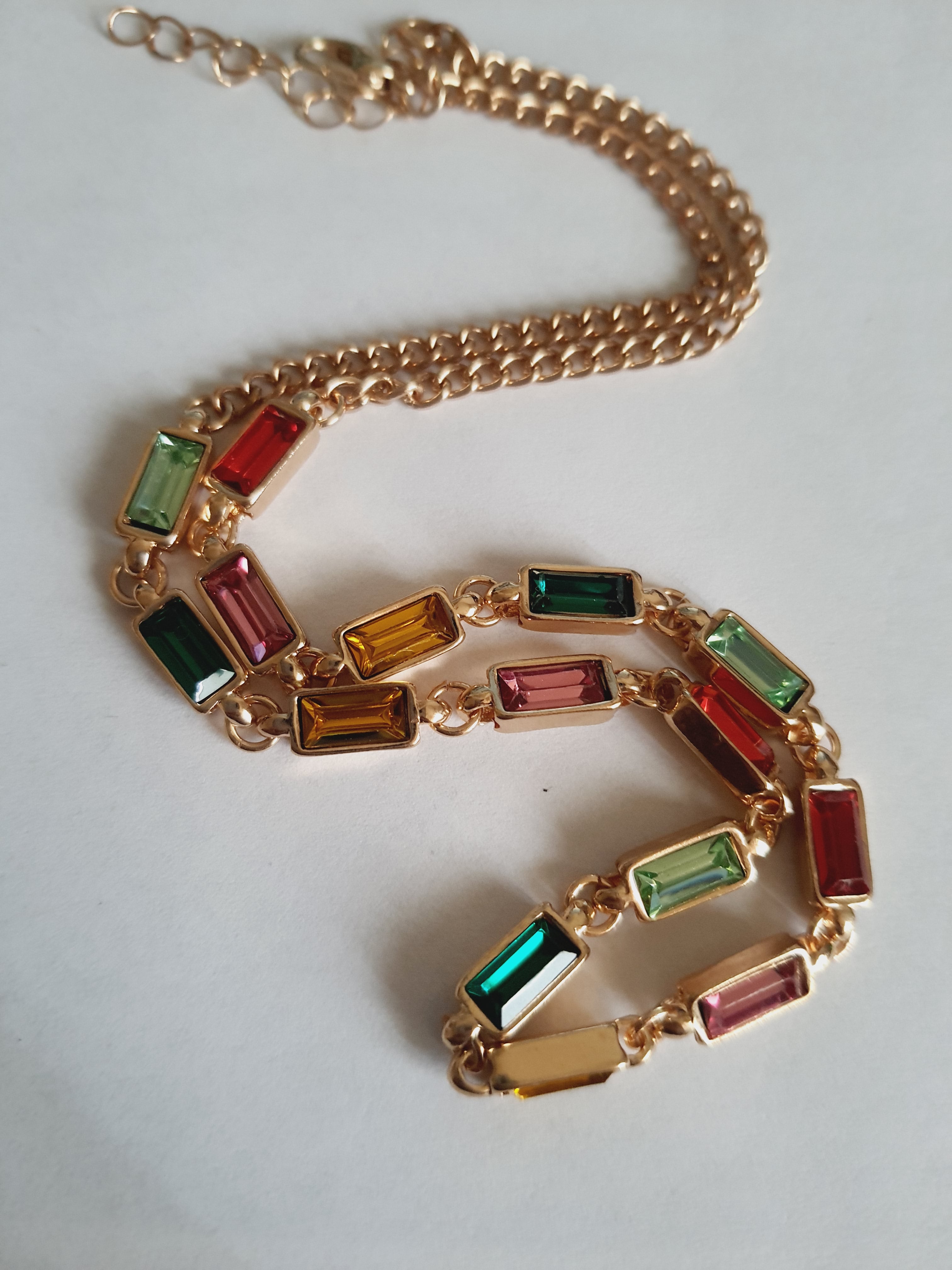 Złoty naszyjnik ze stali nierdzewnej z prostokątnymi, wielobarwnymi kryształami w odcieniach zieleni, czerwieni, różu, złota i turkusu. Długość 41–47 cm. Rouge Bizu.