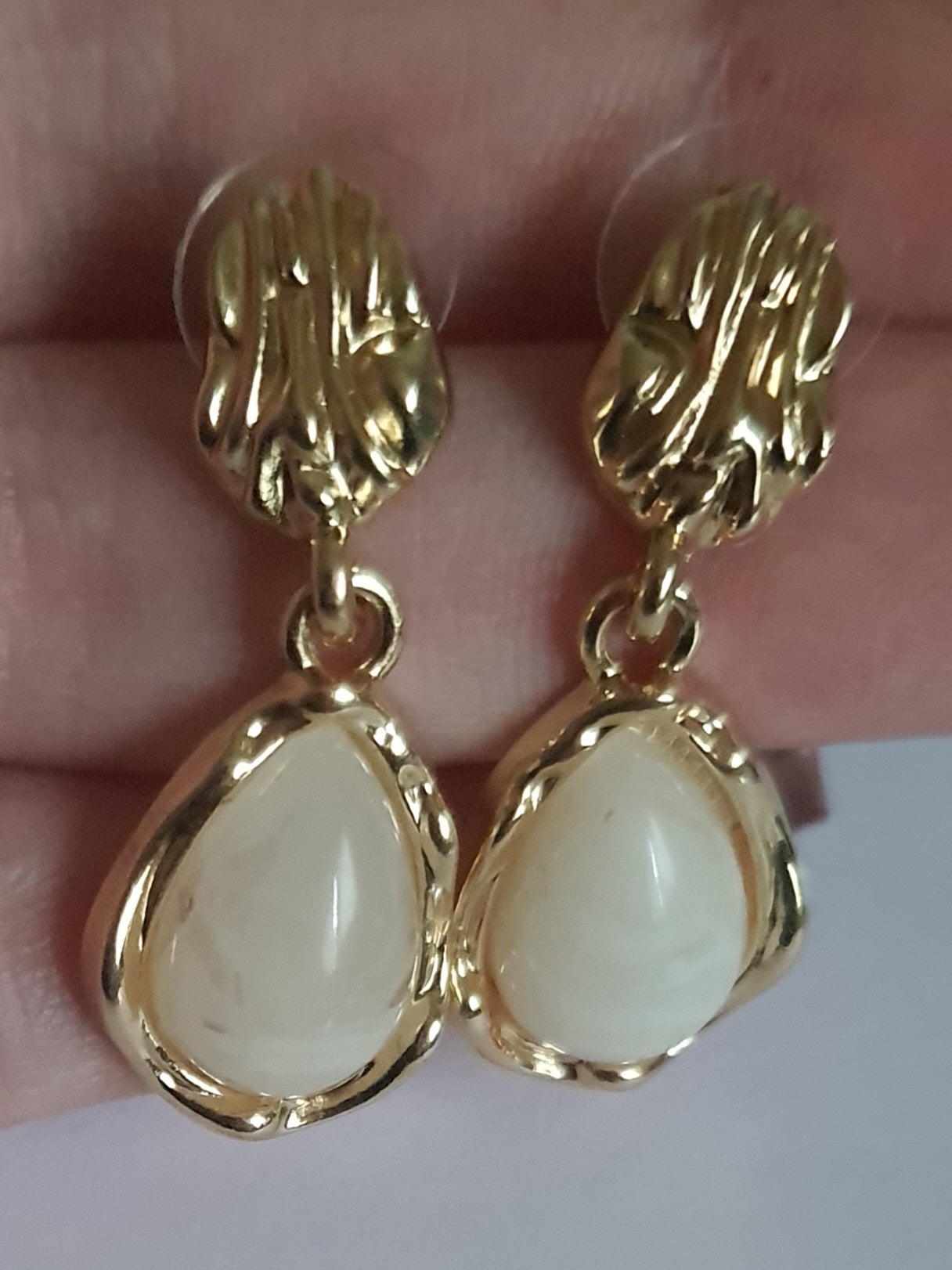 „Złote kolczyki ze stali nierdzewnej o długości 3 cm, zdobione perłowym kaboszonem w kształcie kropli, eleganckie i klasyczne – Rouge Bizu.”