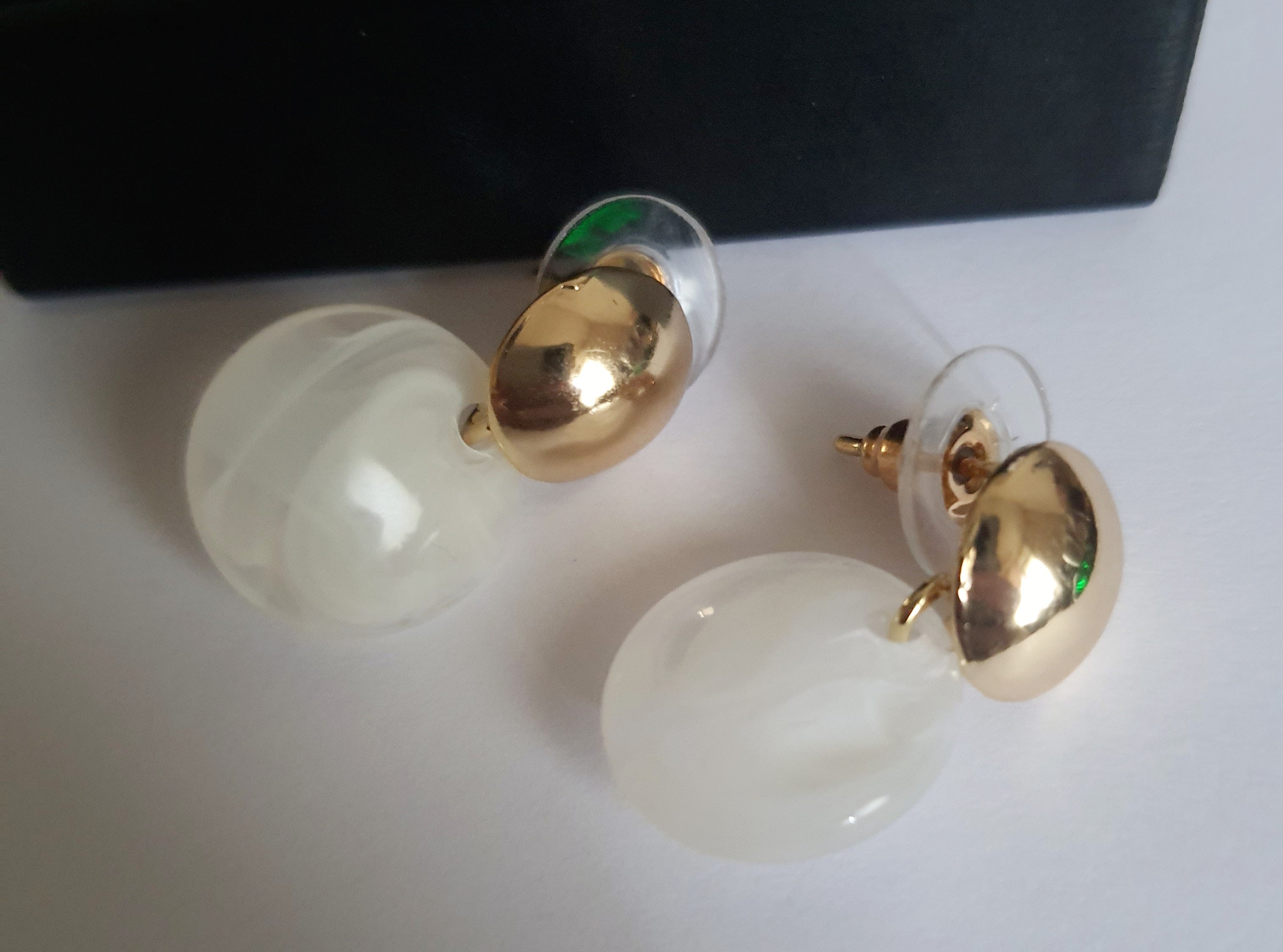 „Złote kolczyki ze stali nierdzewnej o długości 2,5 cm, z perłowym dyskiem zawieszonym na złotym sztyfcie, minimalistyczne i eleganckie – Rouge Bizu.”