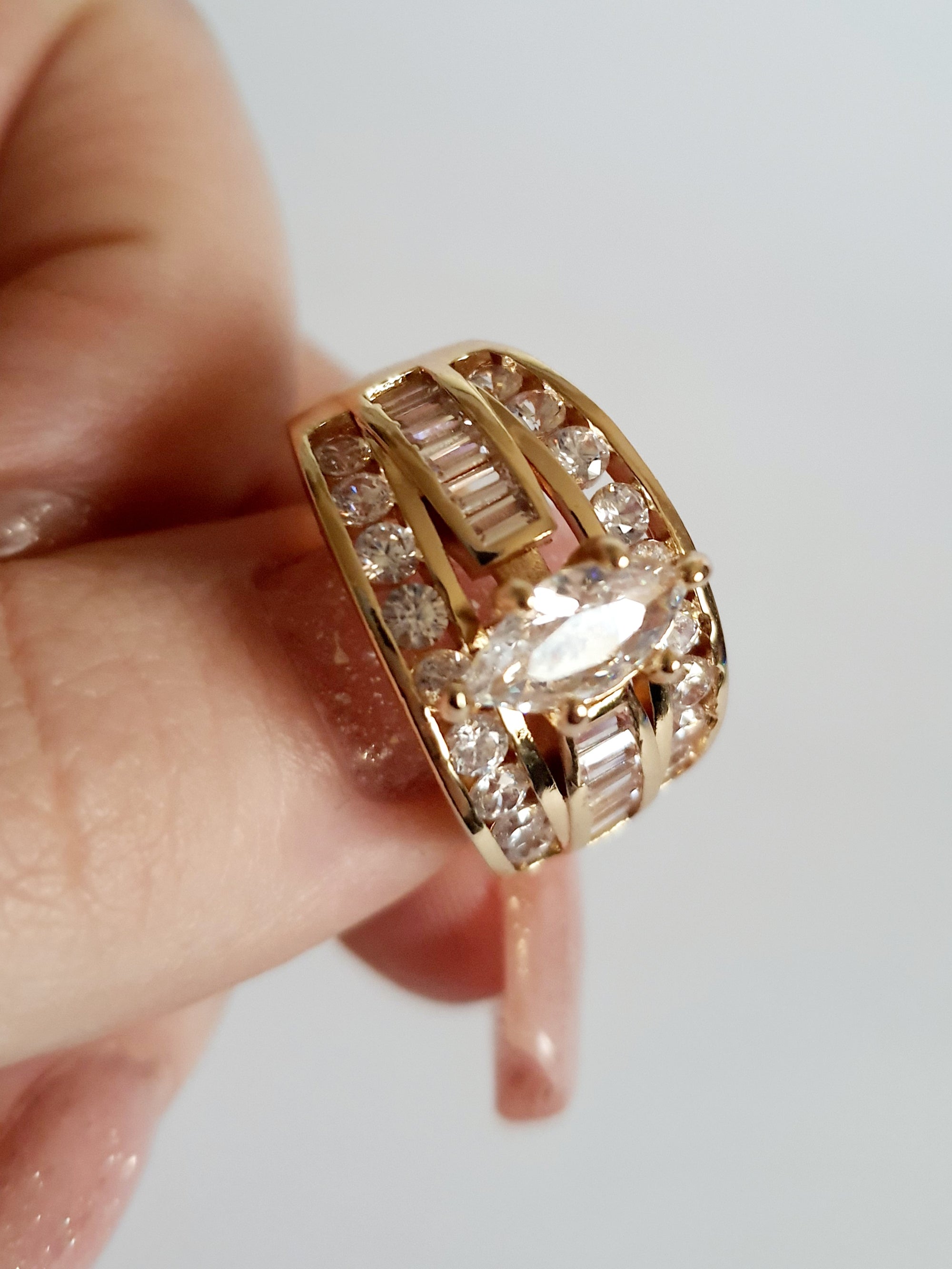 Złoty pierścionek glamour ze stali nierdzewnej, ozdobiony rzędem transparentnych kryształów i centralnym kamieniem w kształcie łezki, rozmiar 19 mm, Rouge Bizu.