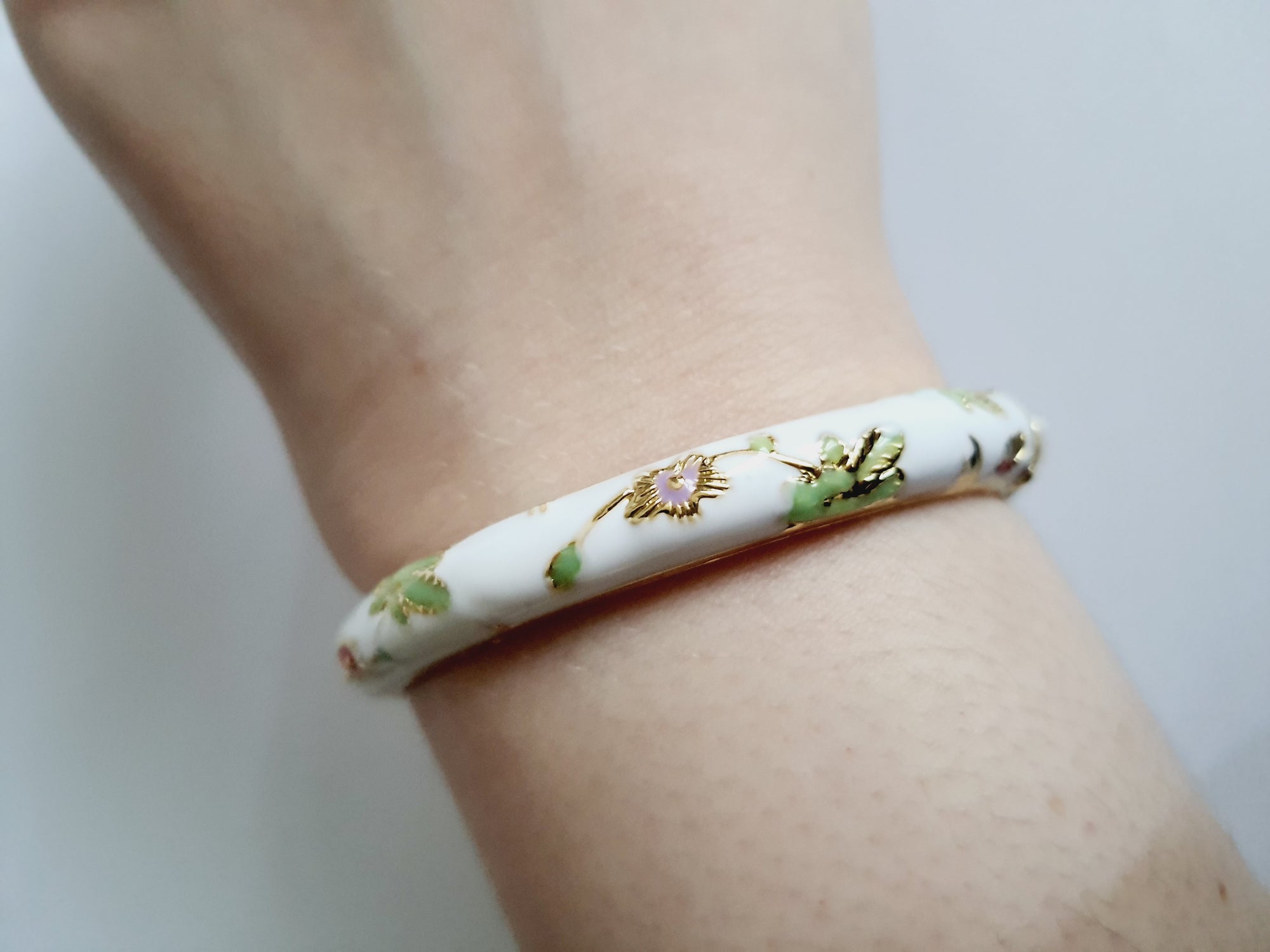 Bransoletka ze stali nierdzewnej, emaliowana na biało, zdobiona złotymi detalami i motywem kwiatowym w kolorach zieleni, czerwieni i różu, średnica 6 cm, Rouge Bizu.