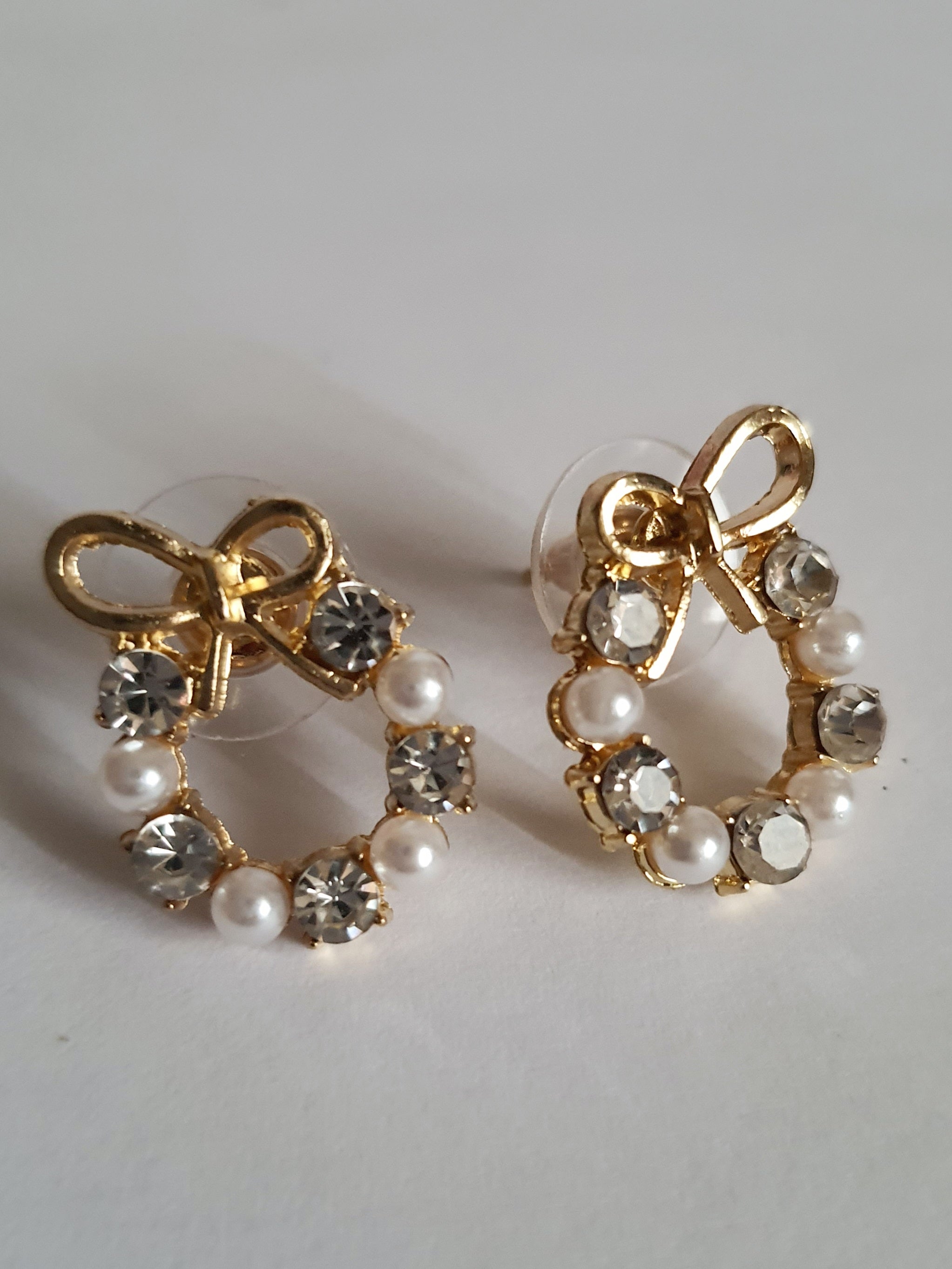 Kolczyki złote ze stali nierdzewnej w kształcie kokardek, zdobione perełkami i transparentnymi kryształkami, długość 2 cm, Rouge Bizu.