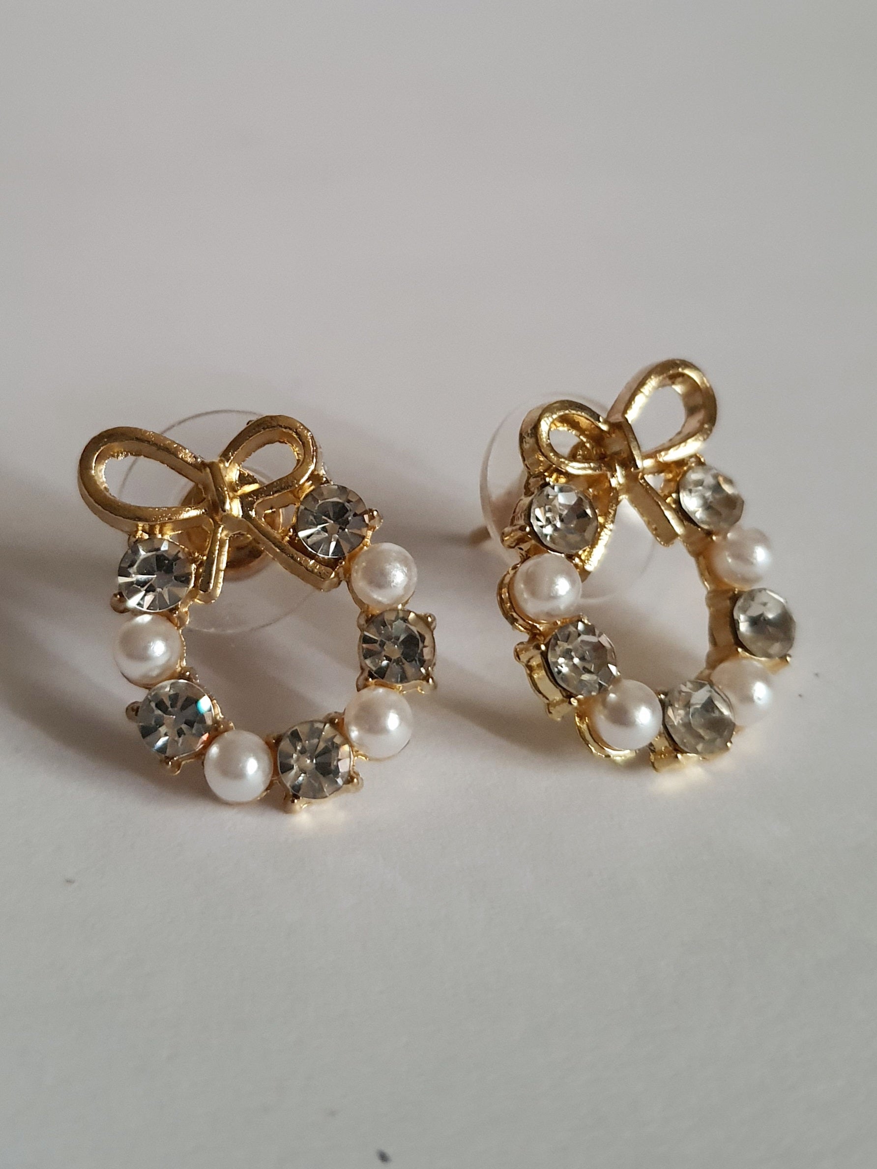 Kolczyki złote ze stali nierdzewnej w kształcie kokardek, zdobione perełkami i transparentnymi kryształkami, długość 2 cm, Rouge Bizu.