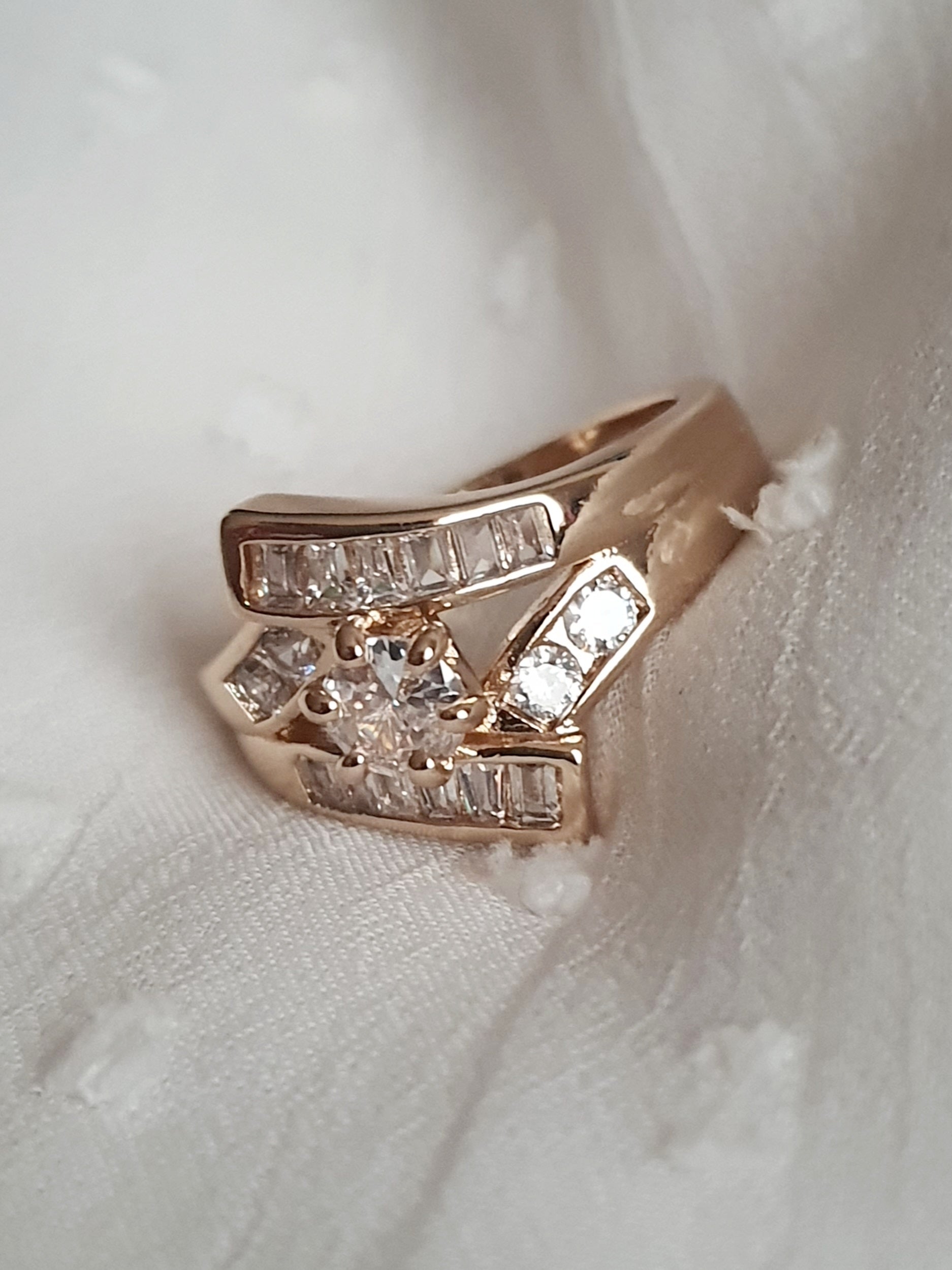 Pierścionek damski ze stali nierdzewnej, złoty, rozmiar 19 mm, zdobiony rzędami prostokątnych cyrkonii i centralnym okrągłym kamieniem, luksusowy styl glamour, Rouge Bizu.