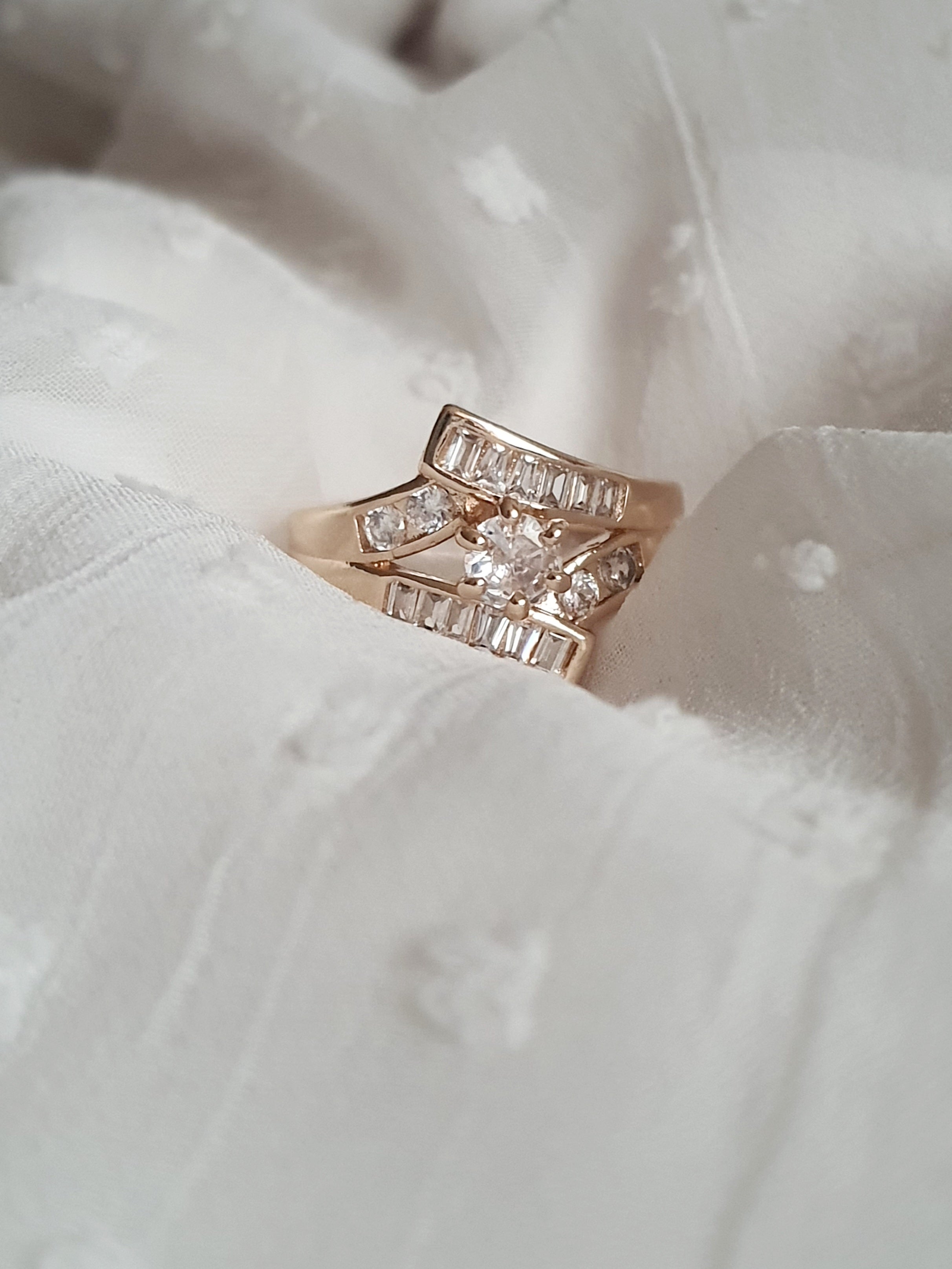 Pierścionek damski ze stali nierdzewnej, złoty, rozmiar 19 mm, zdobiony rzędami prostokątnych cyrkonii i centralnym okrągłym kamieniem, luksusowy styl glamour, Rouge Bizu.