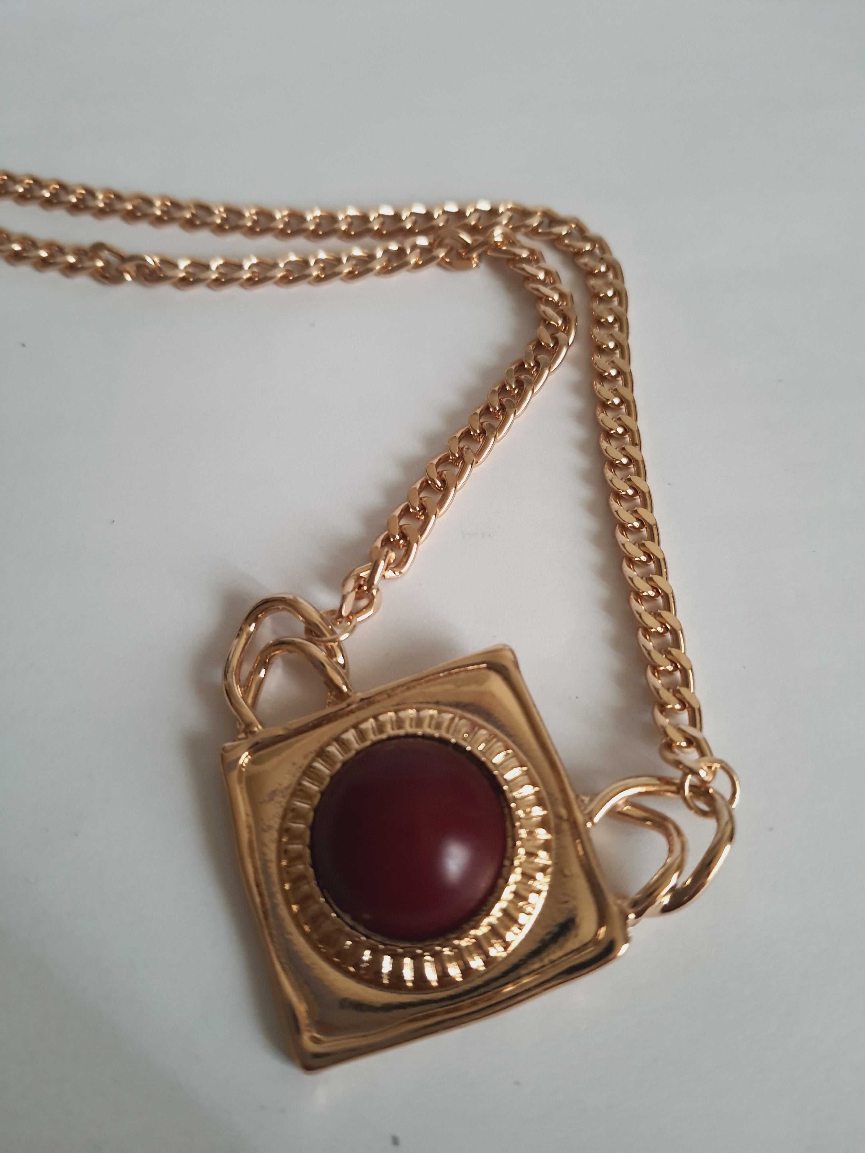 Naszyjnik ze stali nierdzewnej w kolorze złota, z geometryczną zawieszką w kształcie rombu i czerwonym kamieniem pośrodku. Styl elegancki, kobiecy, długość regulowana 44,5–54,5 cm. Rouge Bizu.