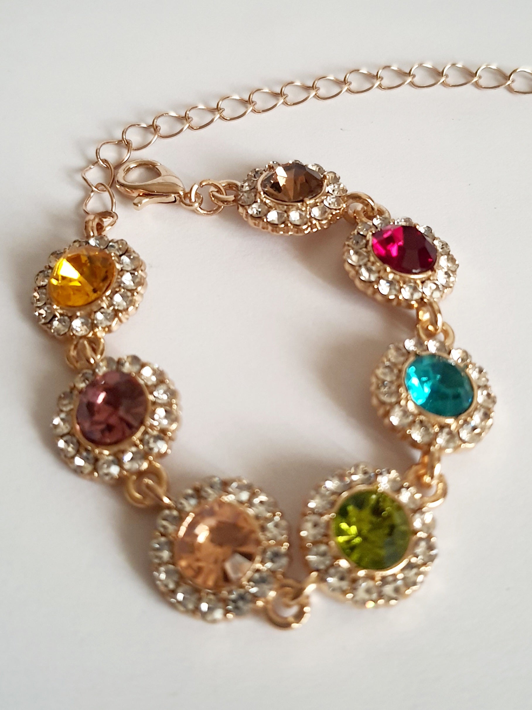 Bransoletka ze stali nierdzewnej w kolorze złota, z okrągłymi kolorowymi kryształami w odcieniach czerwieni, turkusu, zieleni, złota i bursztynu, otoczonymi małymi cyrkoniami. Długość regulowana 25 cm. Rouge Bizu.