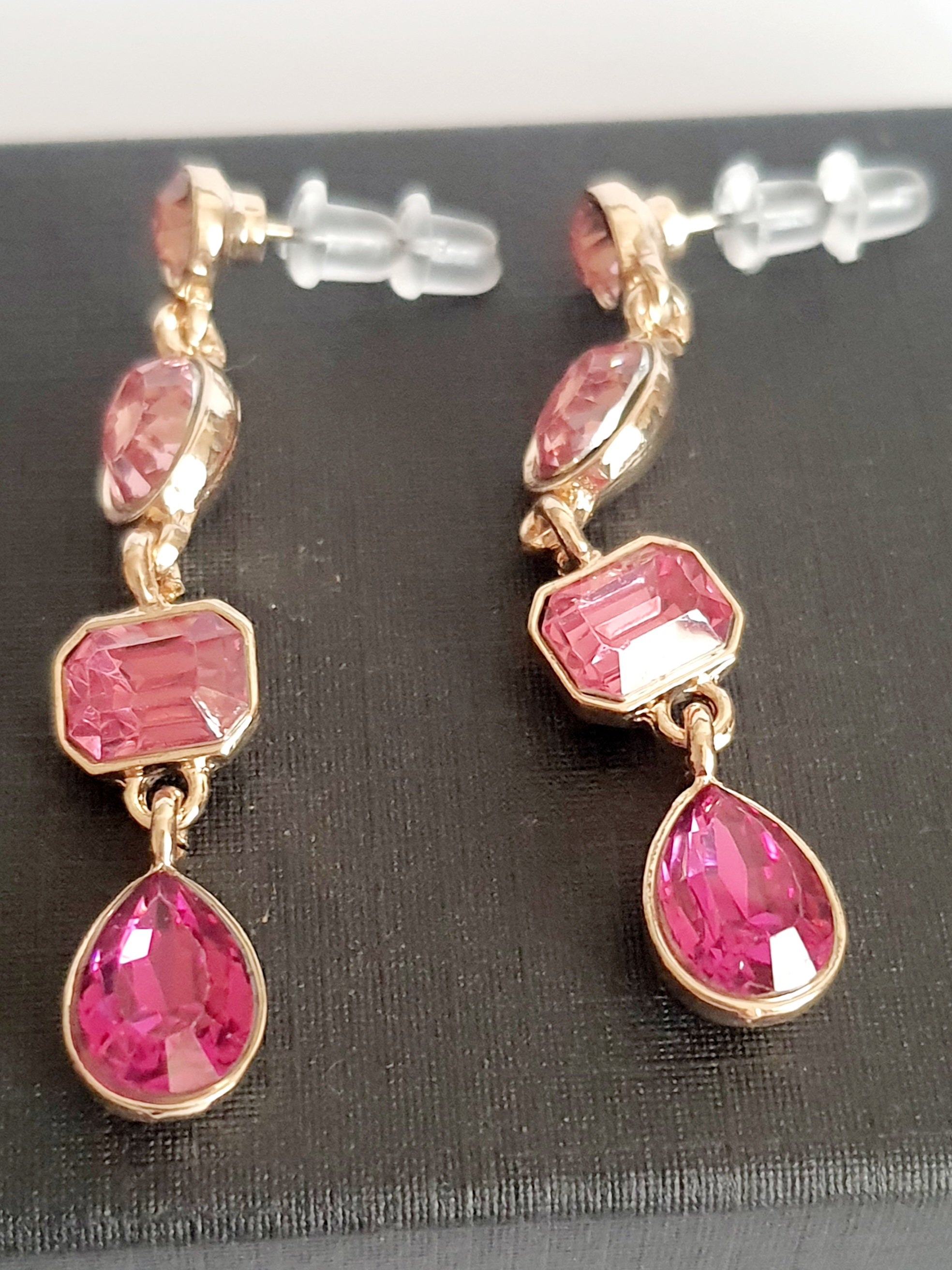 Długie kolczyki wiszące ze stali nierdzewnej w kolorze złota, z różowymi kryształami w kształcie owalu, prostokąta i kropli. Długość 4,5 cm. Styl glamour, elegancki. Rouge Bizu.