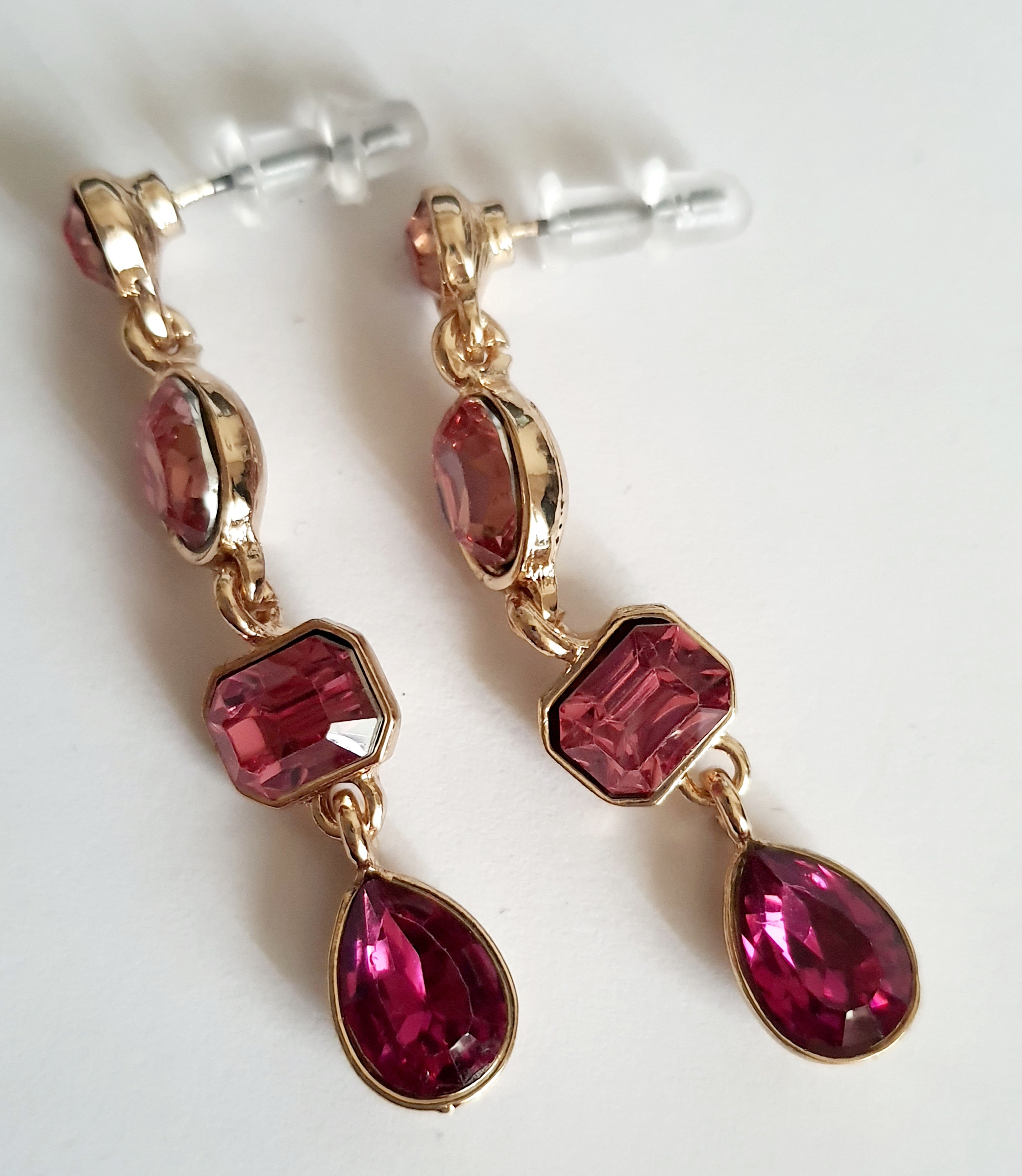 Długie kolczyki wiszące ze stali nierdzewnej w kolorze złota, z różowymi kryształami w kształcie owalu, prostokąta i kropli. Długość 4,5 cm. Styl glamour, elegancki. Rouge Bizu.