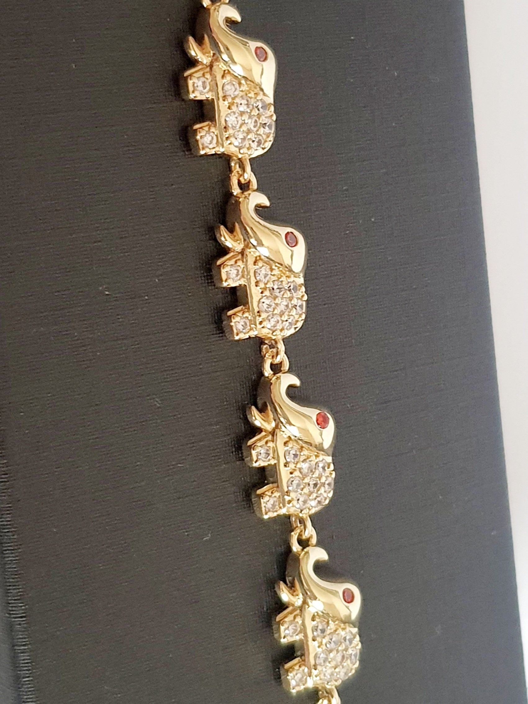Bransoletka ze stali nierdzewnej w kolorze złota z motywem słoni, zdobiona cyrkoniami i czerwonymi oczkami. Symbol szczęścia, długość 20 cm. Rouge Bizu.