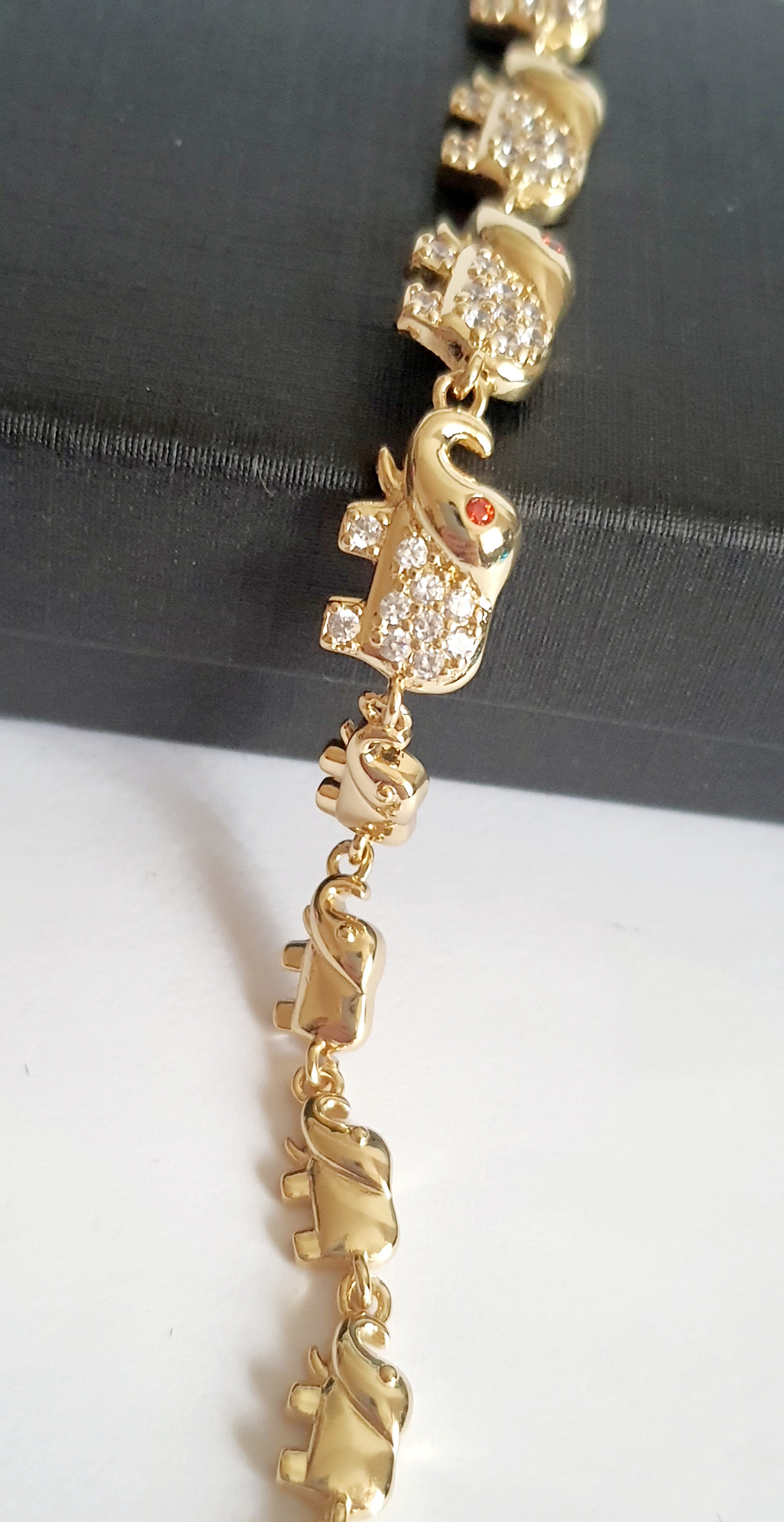 Bransoletka ze stali nierdzewnej w kolorze złota z motywem słoni, zdobiona cyrkoniami i czerwonymi oczkami. Symbol szczęścia, długość 20 cm. Rouge Bizu.