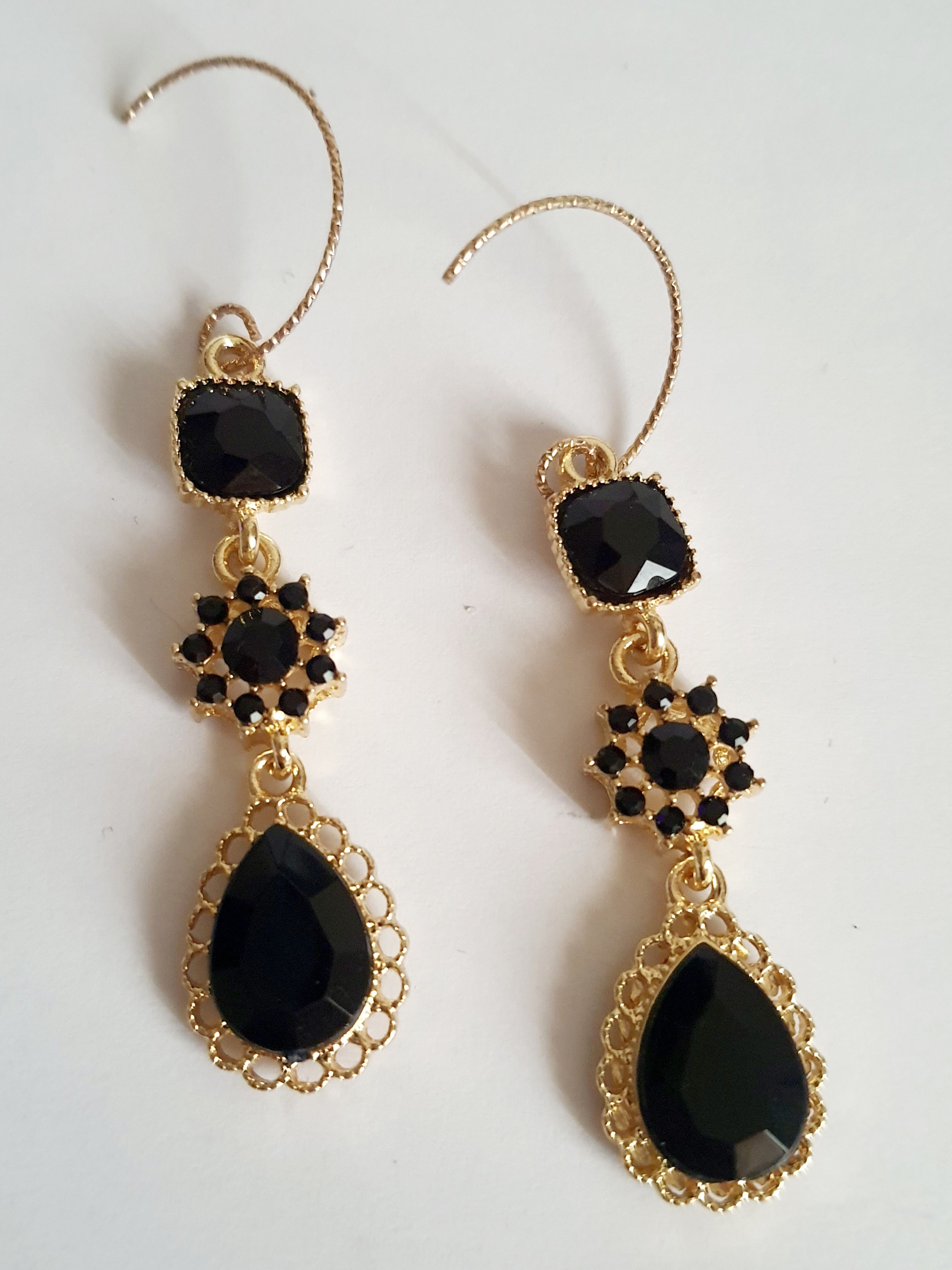 Kolczyki długie ze stali nierdzewnej w kolorze złota z czarnymi kamieniami. Zdobienia w formie kwadratu, rozetki i kropli. Długość 5 cm bez bigla, 6,5 cm z biglem. Styl glamour i elegancki. Rouge Bizu.