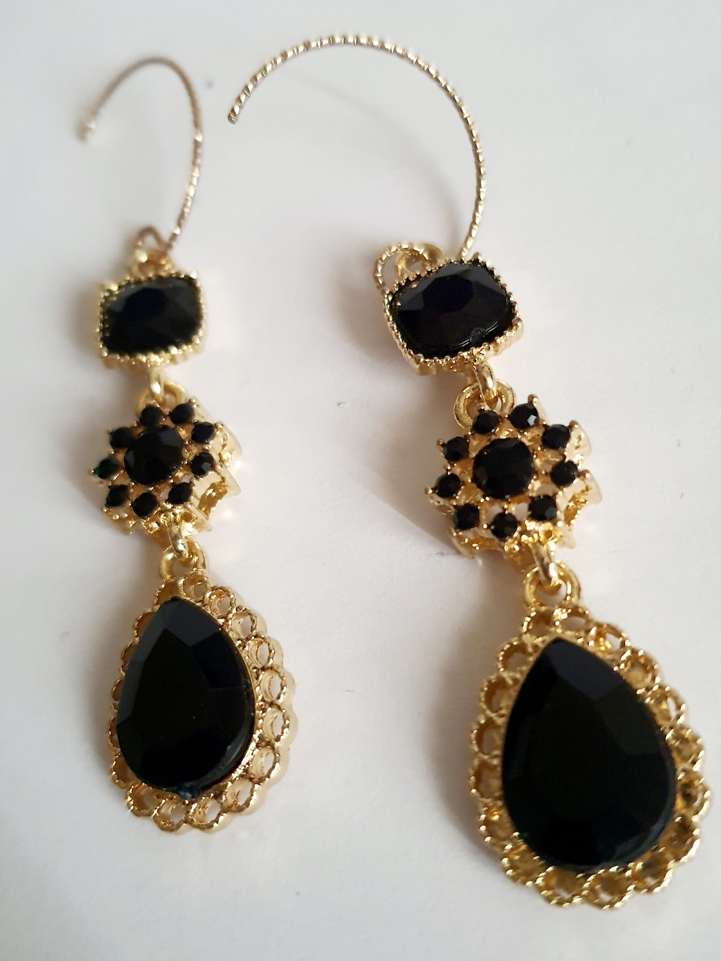 Kolczyki długie ze stali nierdzewnej w kolorze złota z czarnymi kamieniami. Zdobienia w formie kwadratu, rozetki i kropli. Długość 5 cm bez bigla, 6,5 cm z biglem. Styl glamour i elegancki. Rouge Bizu.