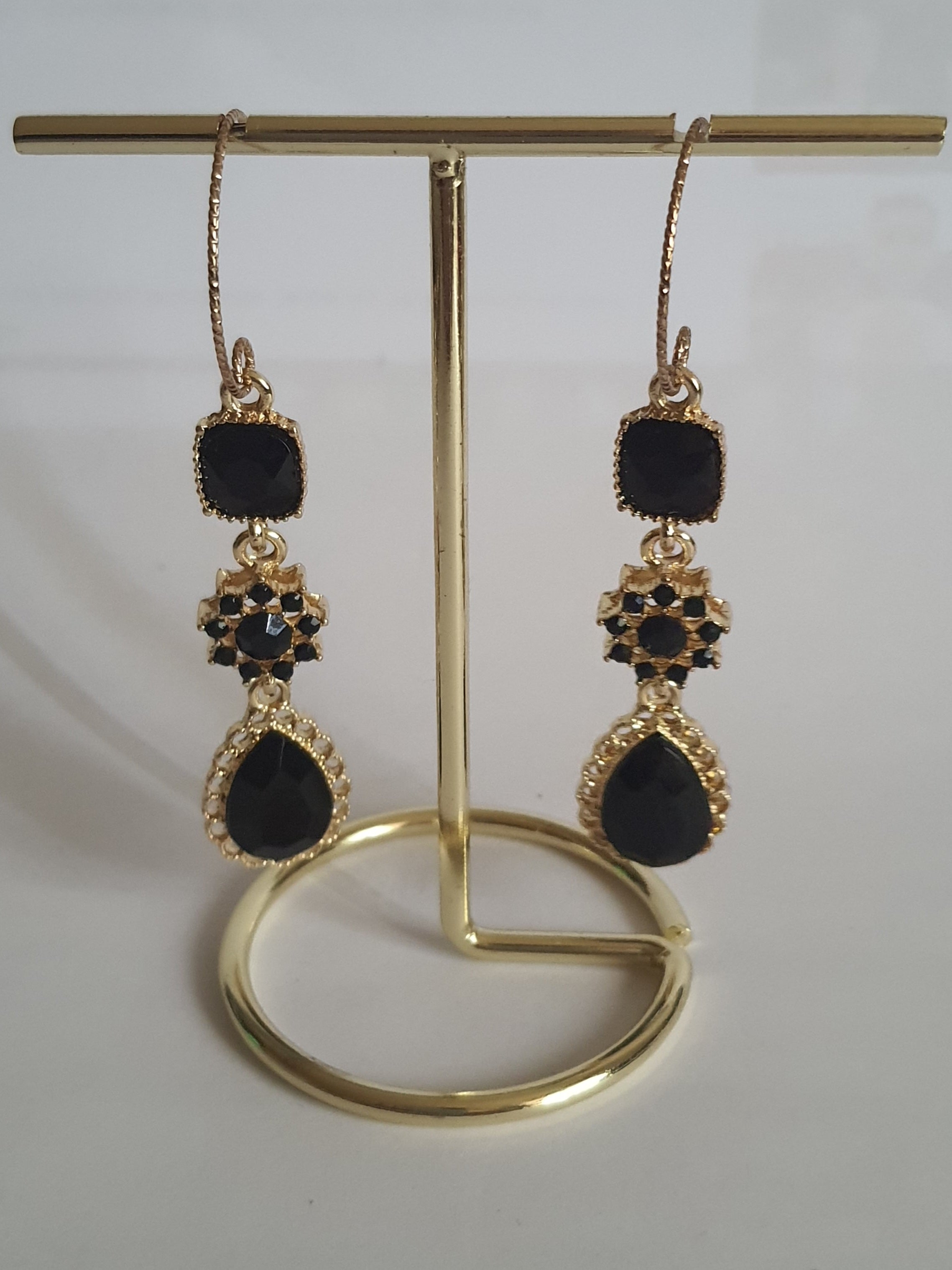 Kolczyki długie ze stali nierdzewnej w kolorze złota z czarnymi kamieniami. Zdobienia w formie kwadratu, rozetki i kropli. Długość 5 cm bez bigla, 6,5 cm z biglem. Styl glamour i elegancki. Rouge Bizu.