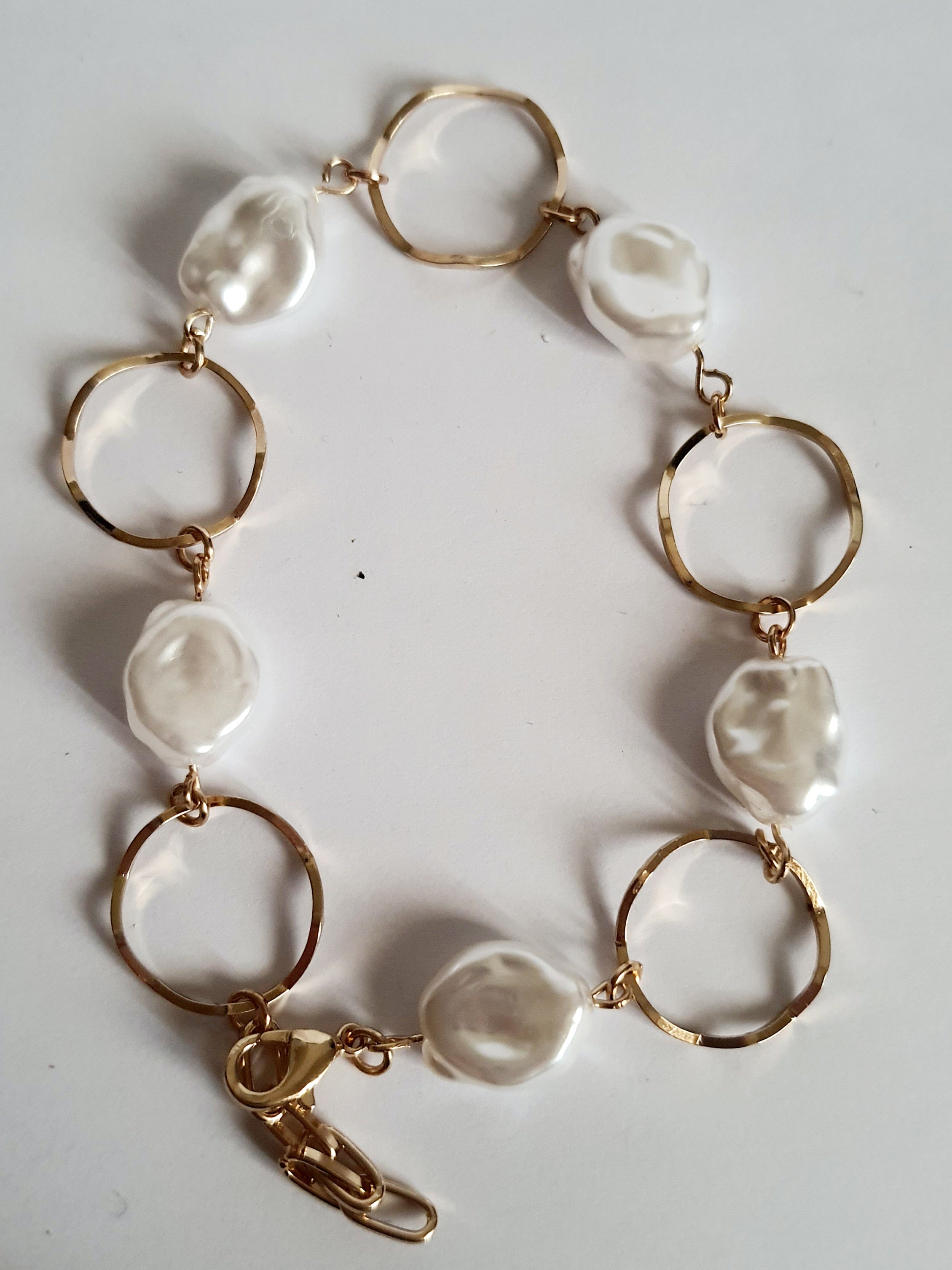 Bransoletka ze stali nierdzewnej w kolorze złota, z nieregularnymi białymi perłami i złotymi kołami. Regulowana długość 22–26 cm. Styl elegancki i minimalistyczny. Rouge Bizu.