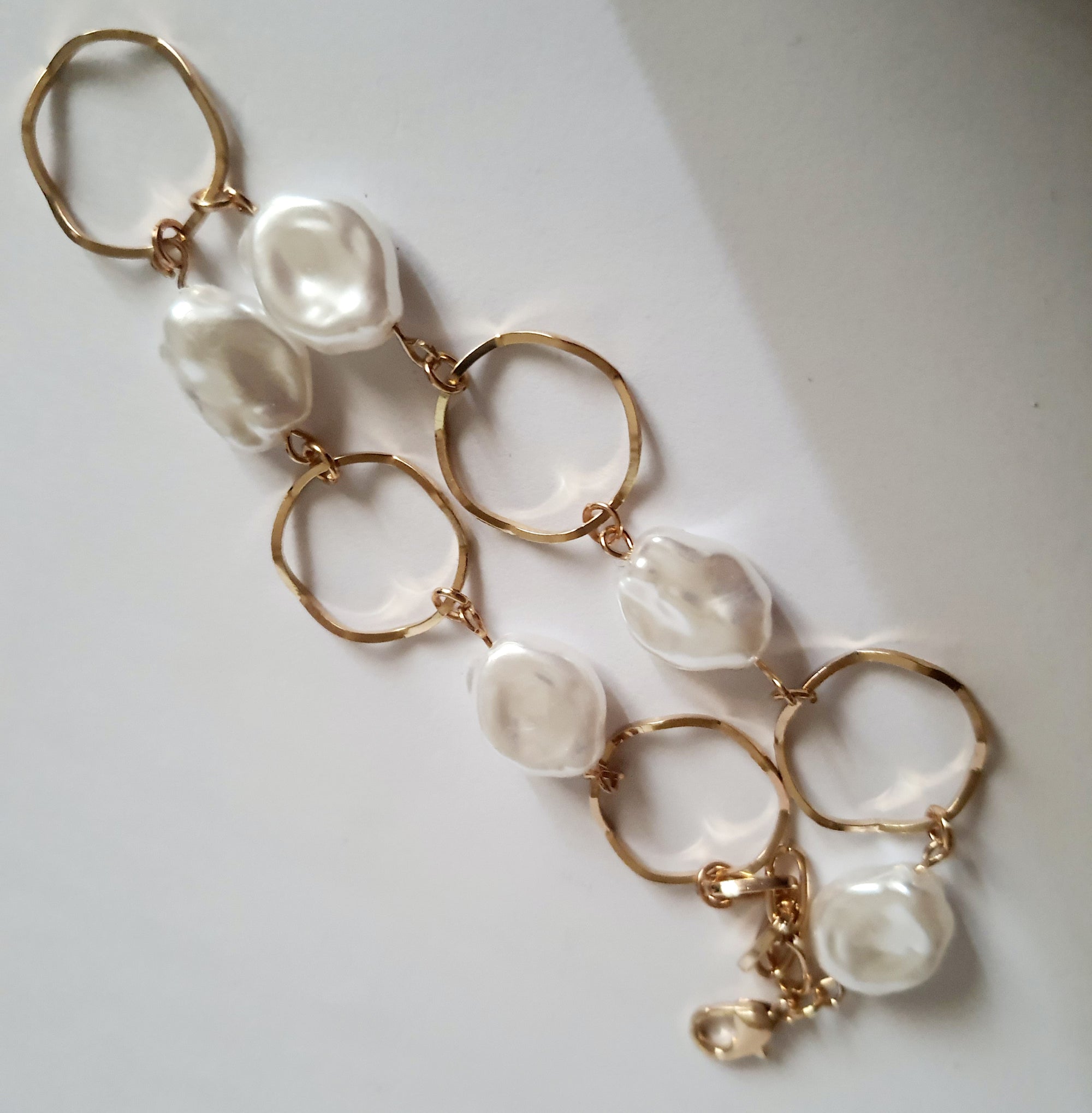Bransoletka ze stali nierdzewnej w kolorze złota, z nieregularnymi białymi perłami i złotymi kołami. Regulowana długość 22–26 cm. Styl elegancki i minimalistyczny. Rouge Bizu.