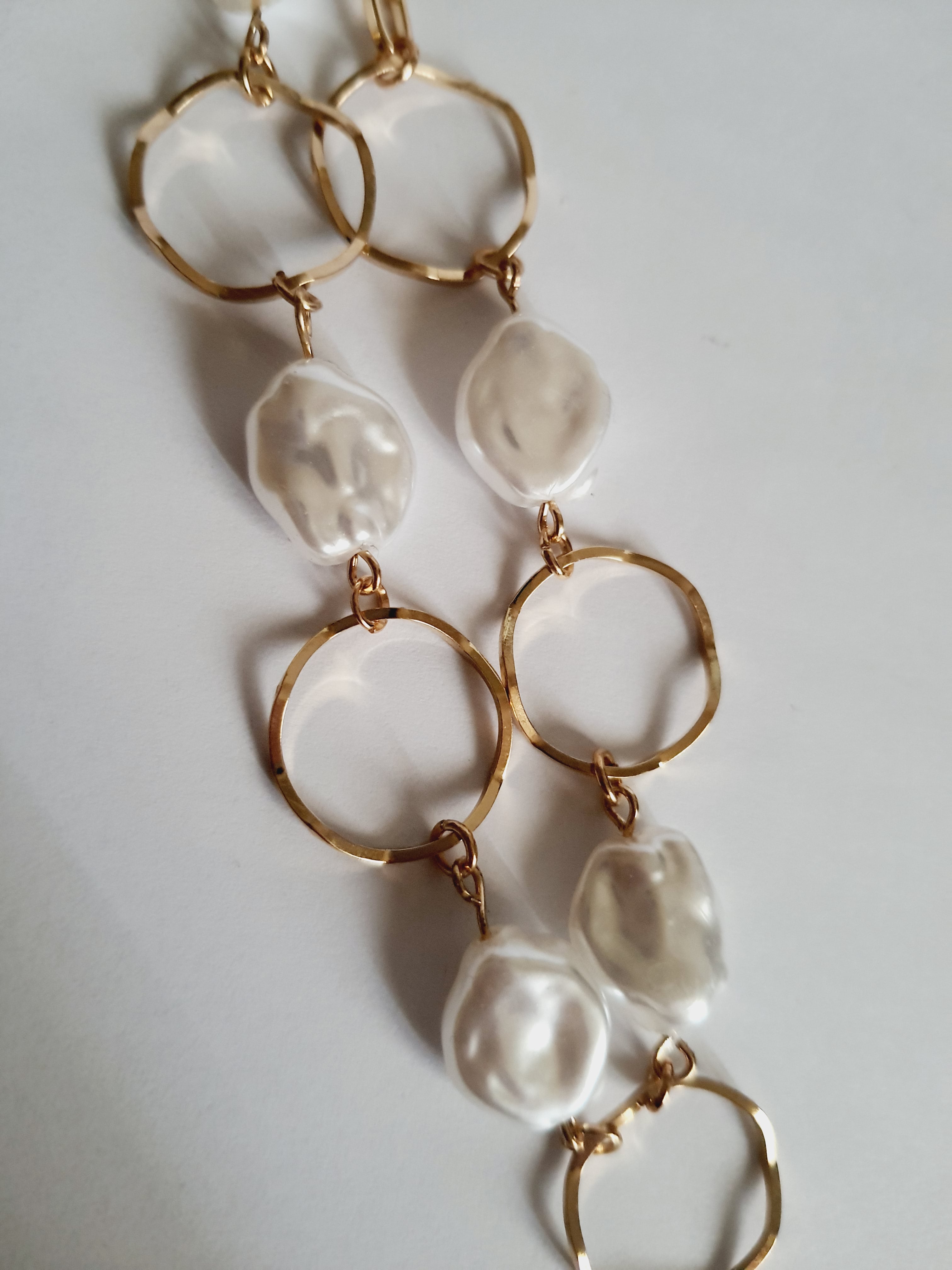 Bransoletka ze stali nierdzewnej w kolorze złota, z nieregularnymi białymi perłami i złotymi kołami. Regulowana długość 22–26 cm. Styl elegancki i minimalistyczny. Rouge Bizu.