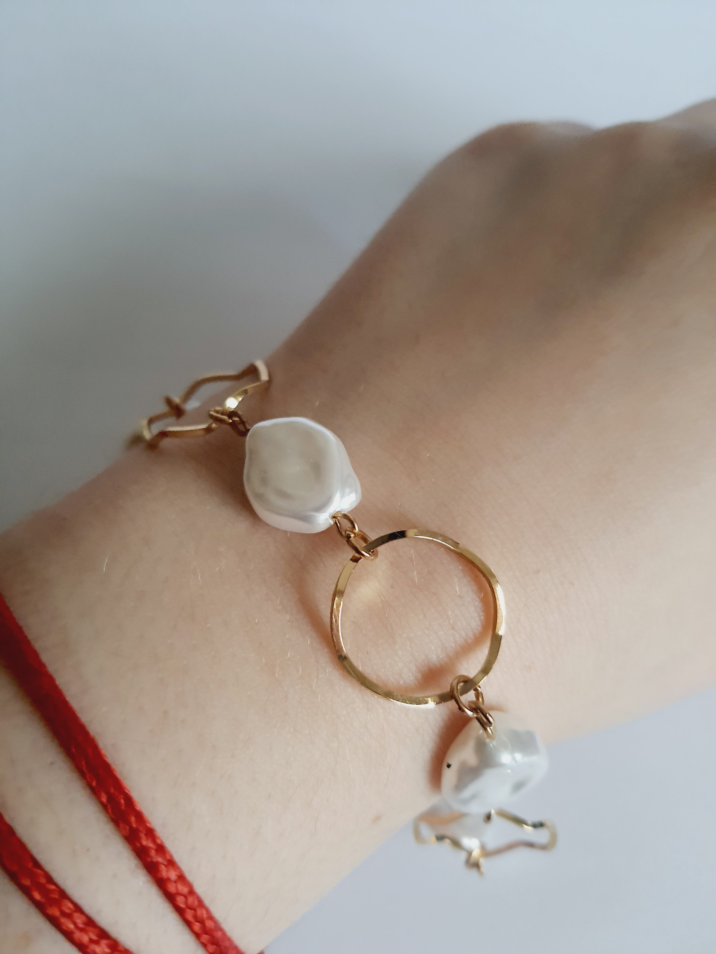 Bransoletka ze stali nierdzewnej w kolorze złota, z nieregularnymi białymi perłami i złotymi kołami. Regulowana długość 22–26 cm. Styl elegancki i minimalistyczny. Rouge Bizu.