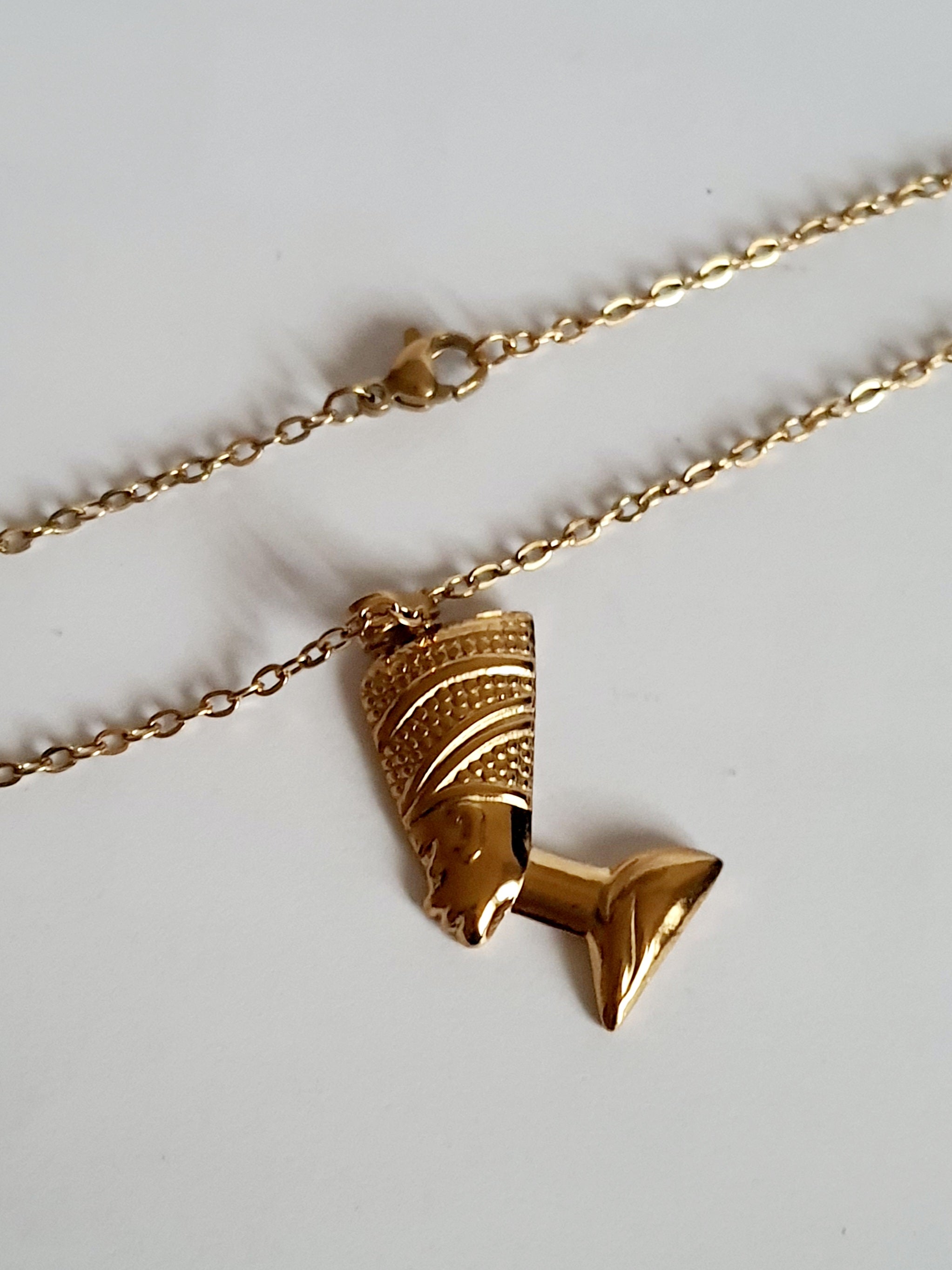 Naszyjnik ze stali nierdzewnej w kolorze złota, z zawieszką przedstawiającą profil królowej w koronie. Długość 50 cm. Styl elegancki i symboliczny. Rouge Bizu.