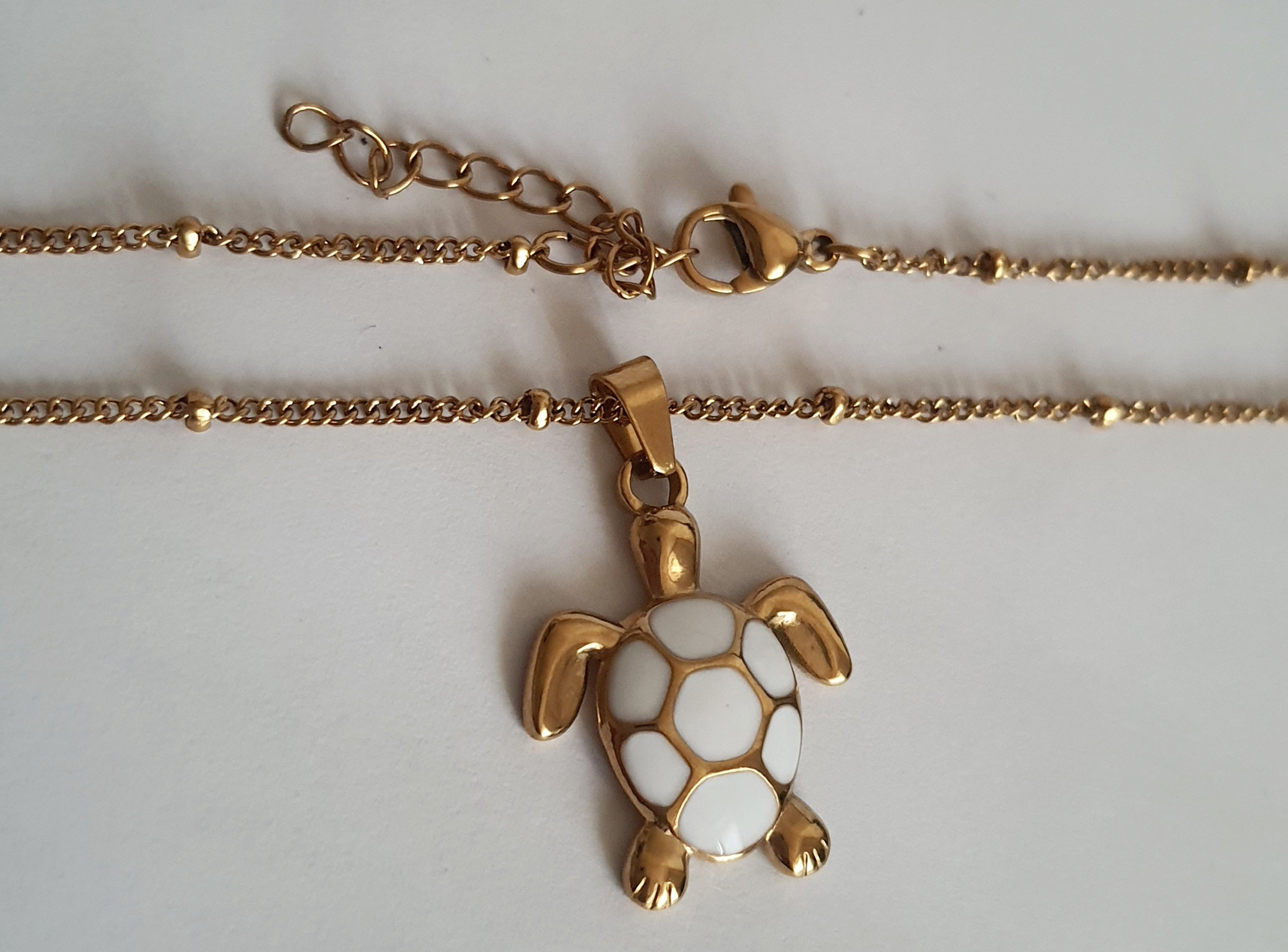 Naszyjnik złoty 40–45 cm ze stali nierdzewnej, zawieszka żółw z białą emalią na pancerzu, symboliczna i elegancka biżuteria, Rouge Bizu.#bizuteria #biżuteriapozłacana #stalnierdzewna #stalchirurgiczna #platerowane18k #wodoodporne #hipoalergiczne #retro #vintage #złotynaszyjnik #rougebizu