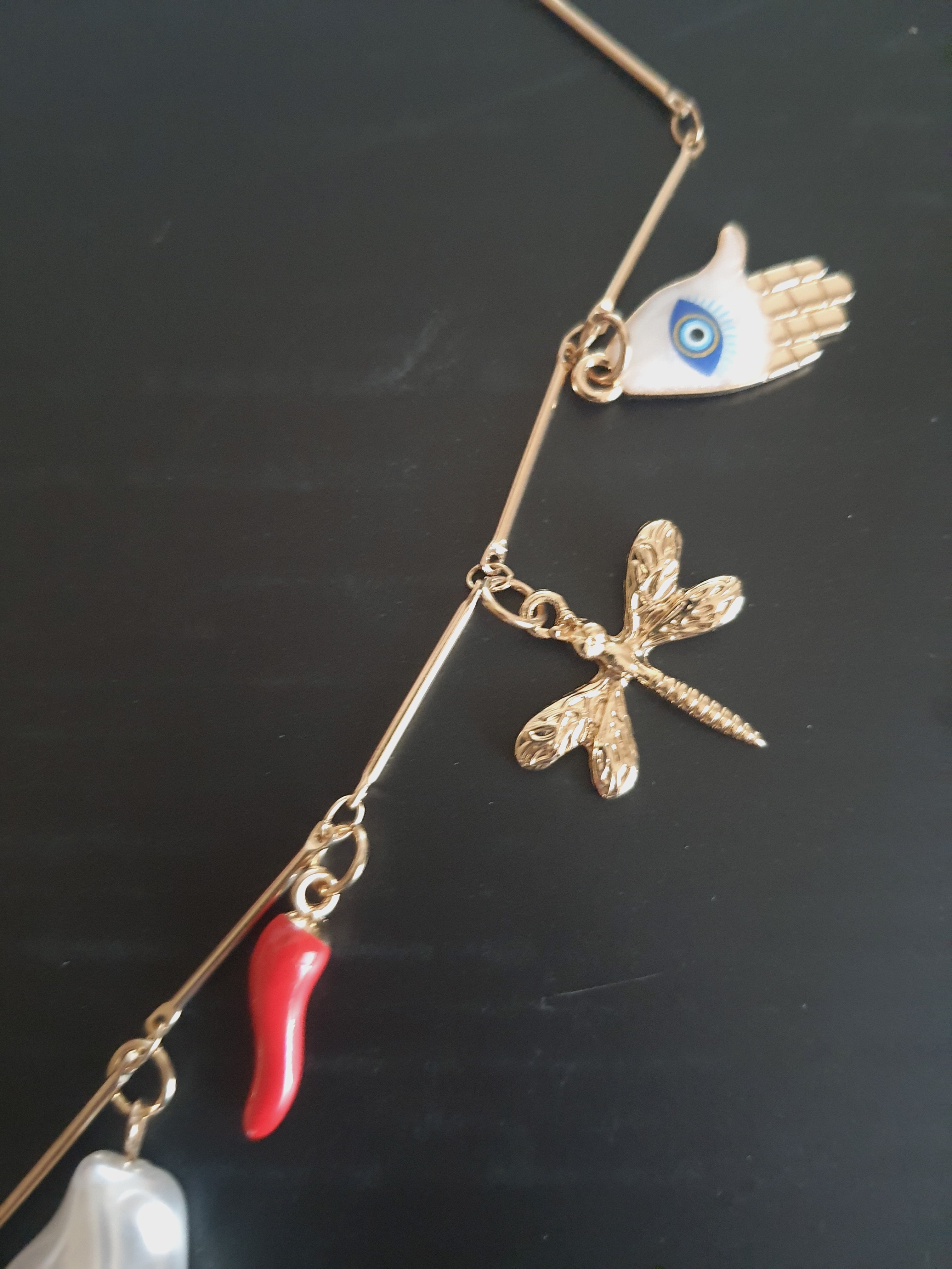 Złoty naszyjnik ze stali chirurgicznej z charmsami – sercem, biedronką, perłą syntetyczną, krzyżykiem, okiem proroczym, dłonią Fatimy, ważką i innymi symbolami. Regulowana długość 45–50 cm. Stal chirurgiczna, stal nierdzewna, wodoodporne, hipoalergiczne, jakość premium. RougeBizu.