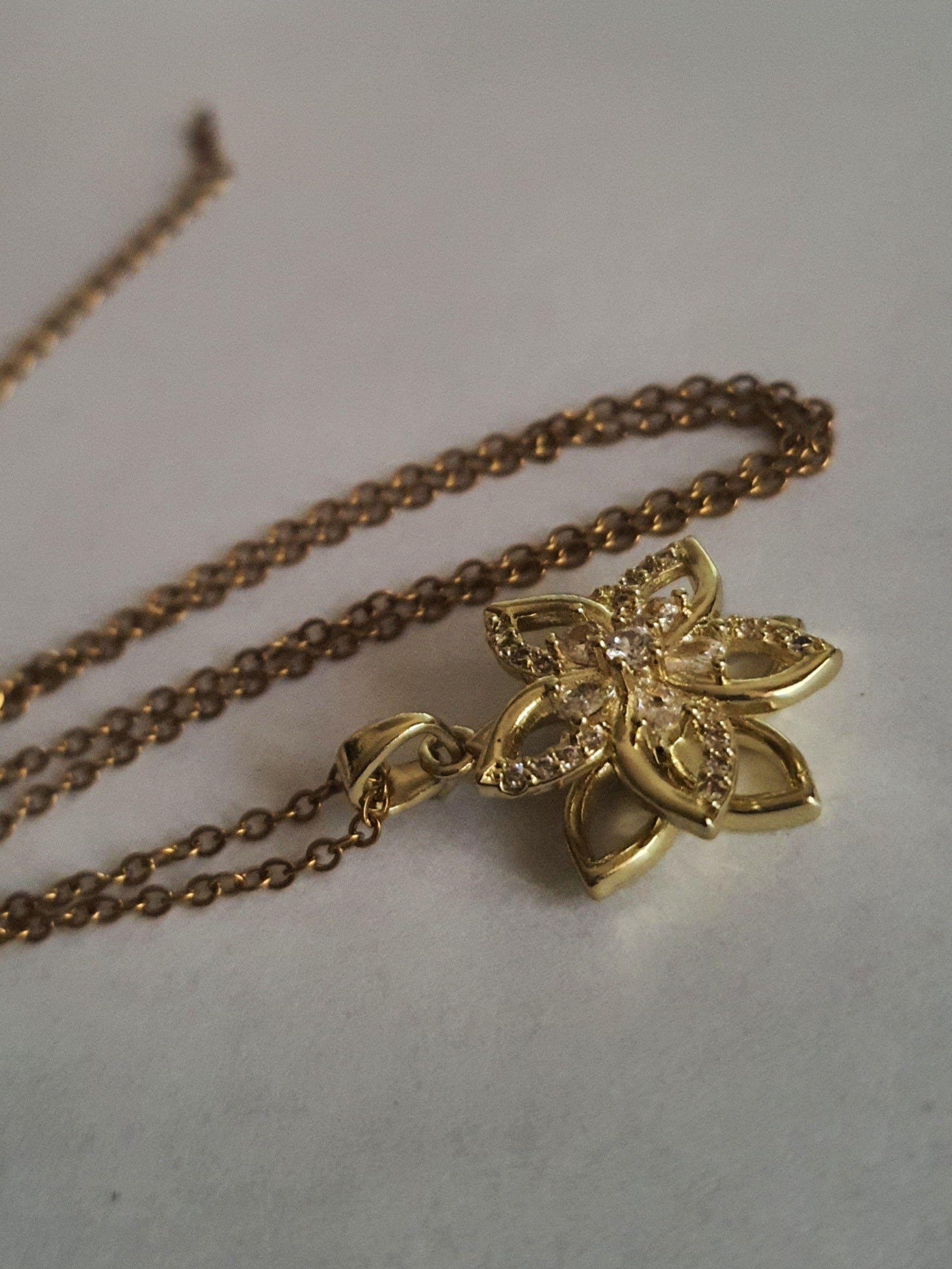 Złoty naszyjnik ze stali chirurgicznej z zawieszką w kształcie kwiatowej rozety wysadzanej cyrkoniami. Regulowana długość 45–50 cm. Stal chirurgiczna, stal nierdzewna, wodoodporne, hipoalergiczne, jakość premium. RougeBizu.