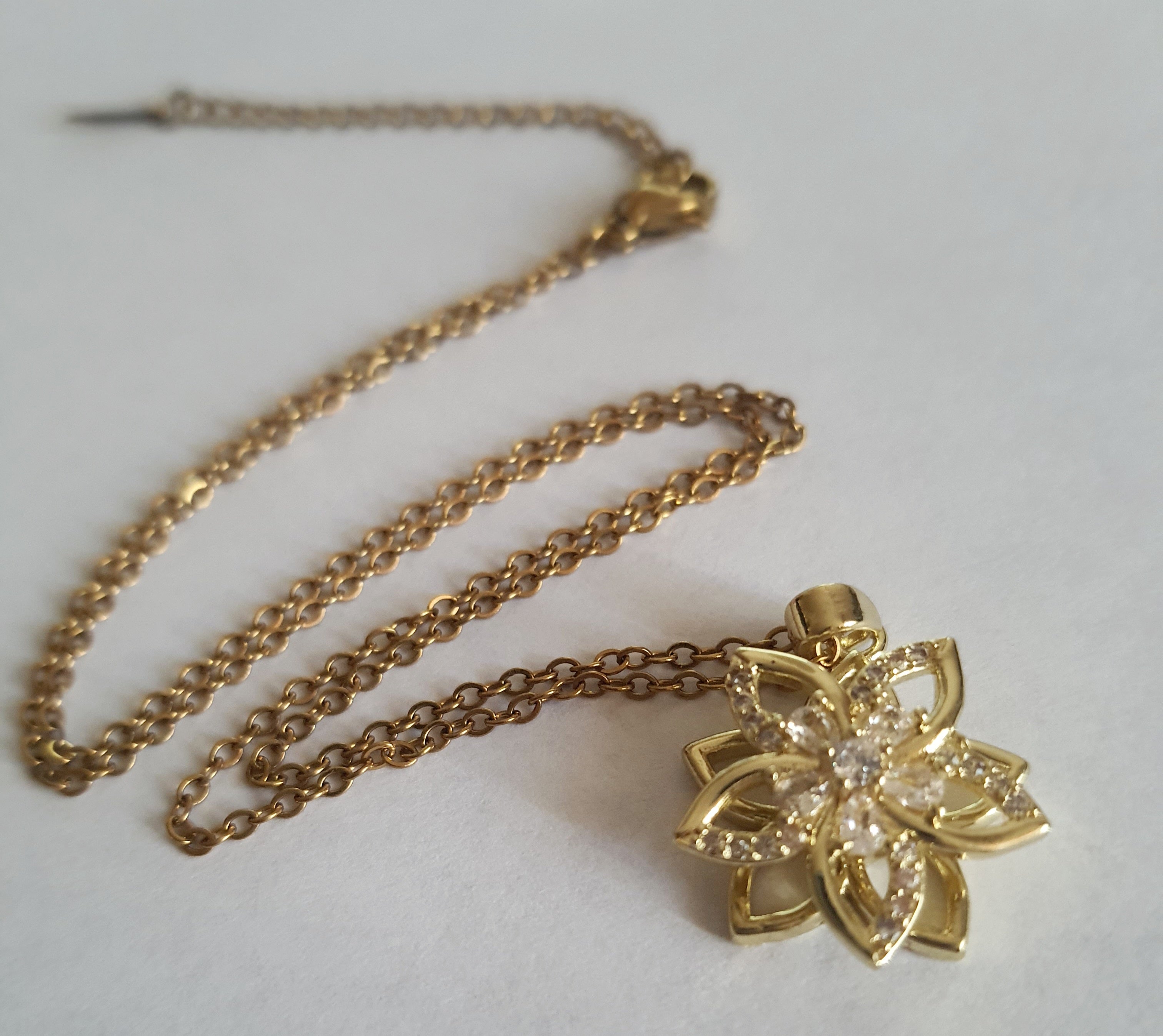 Złoty naszyjnik ze stali chirurgicznej z zawieszką w kształcie kwiatowej rozety wysadzanej cyrkoniami. Regulowana długość 45–50 cm. Stal chirurgiczna, stal nierdzewna, wodoodporne, hipoalergiczne, jakość premium. RougeBizu.