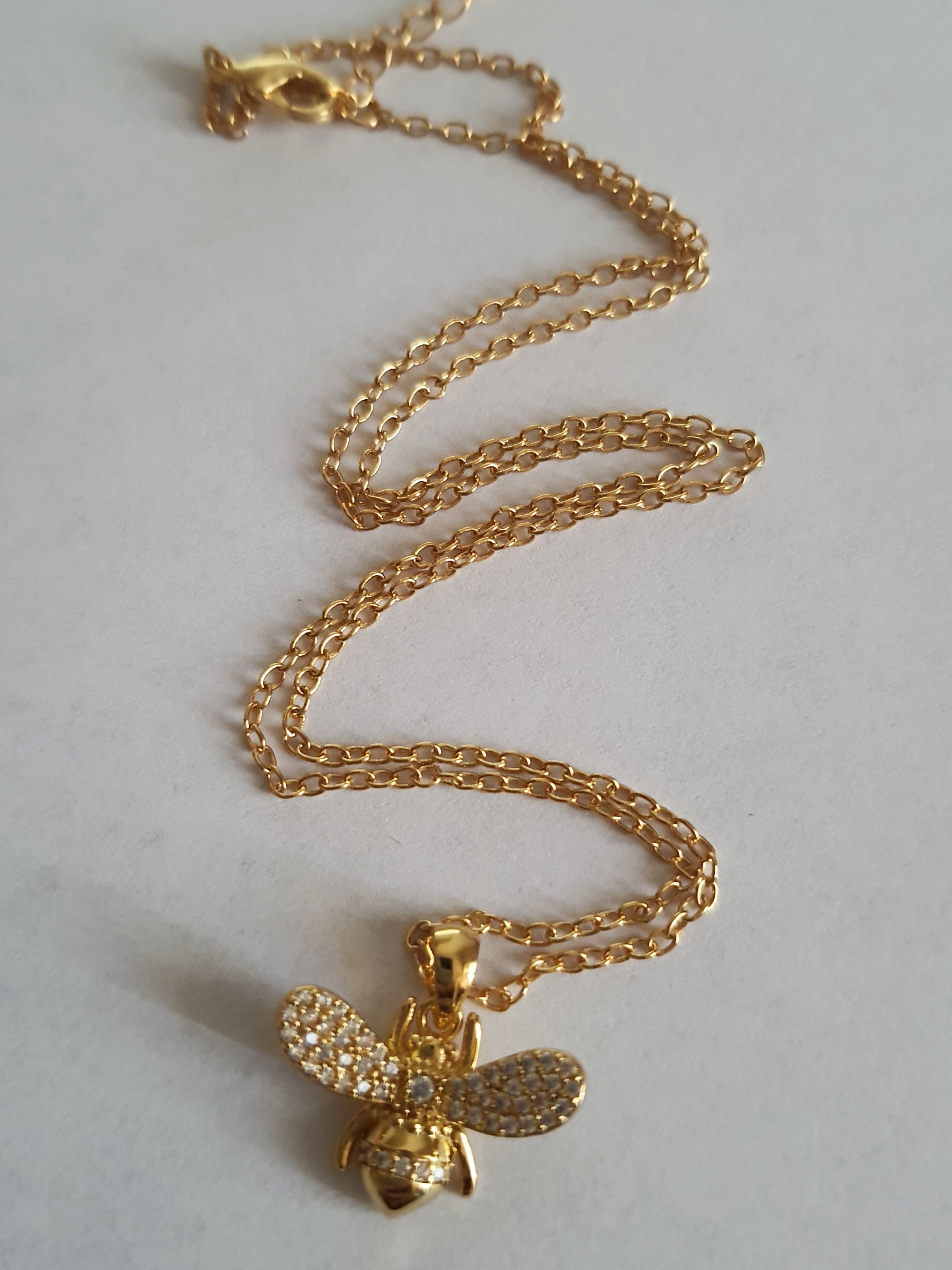 Złoty naszyjnik ze stali chirurgicznej z zawieszką w kształcie pszczółki wysadzanej cyrkoniami. Regulowana długość 40–45 cm. Stal chirurgiczna, stal nierdzewna, wodoodporne, hipoalergiczne, jakość premium. RougeBizu.