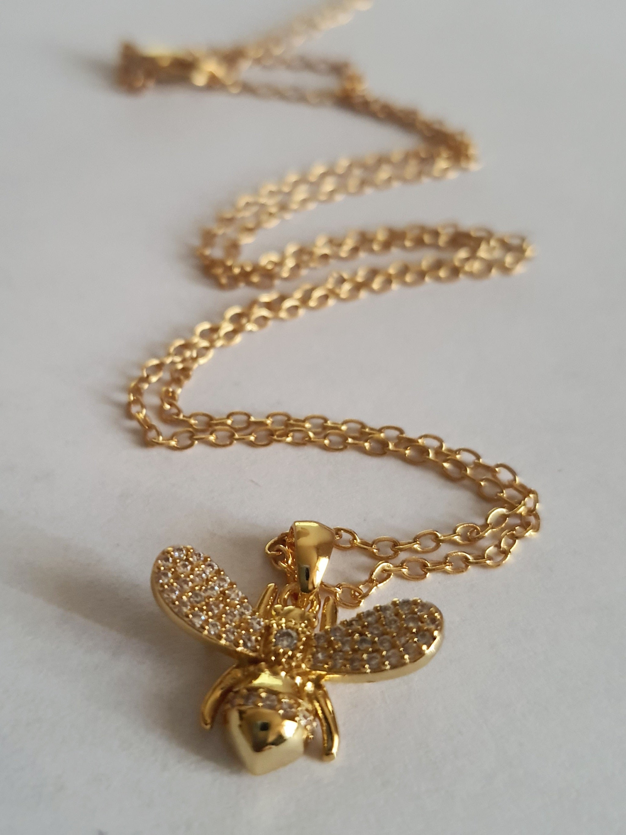 Złoty naszyjnik ze stali chirurgicznej z zawieszką w kształcie pszczółki wysadzanej cyrkoniami. Regulowana długość 40–45 cm. Stal chirurgiczna, stal nierdzewna, wodoodporne, hipoalergiczne, jakość premium. RougeBizu.